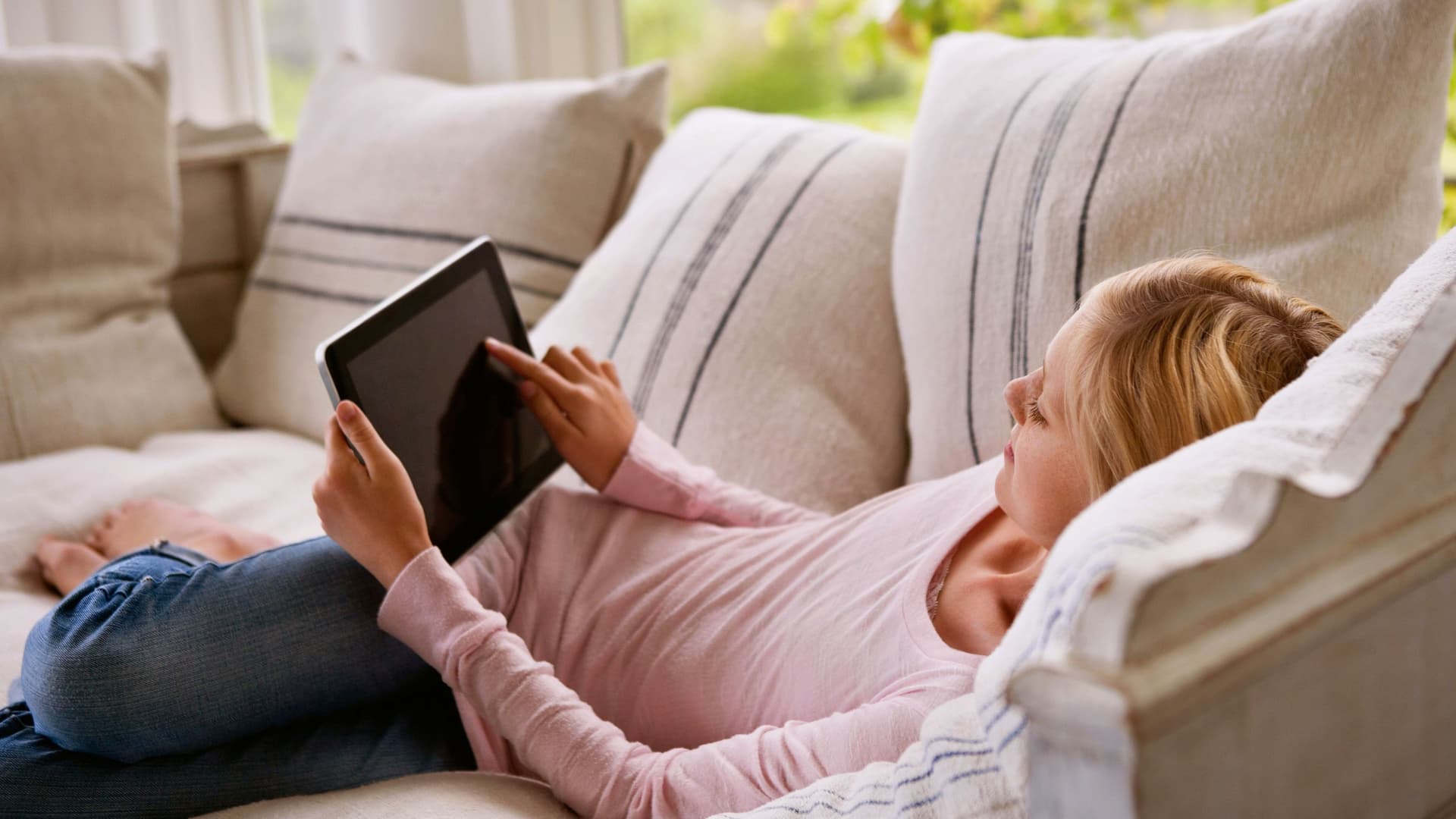 Eine Junge Frau liegt auf einem Sofa und benutzt ein Tablet
