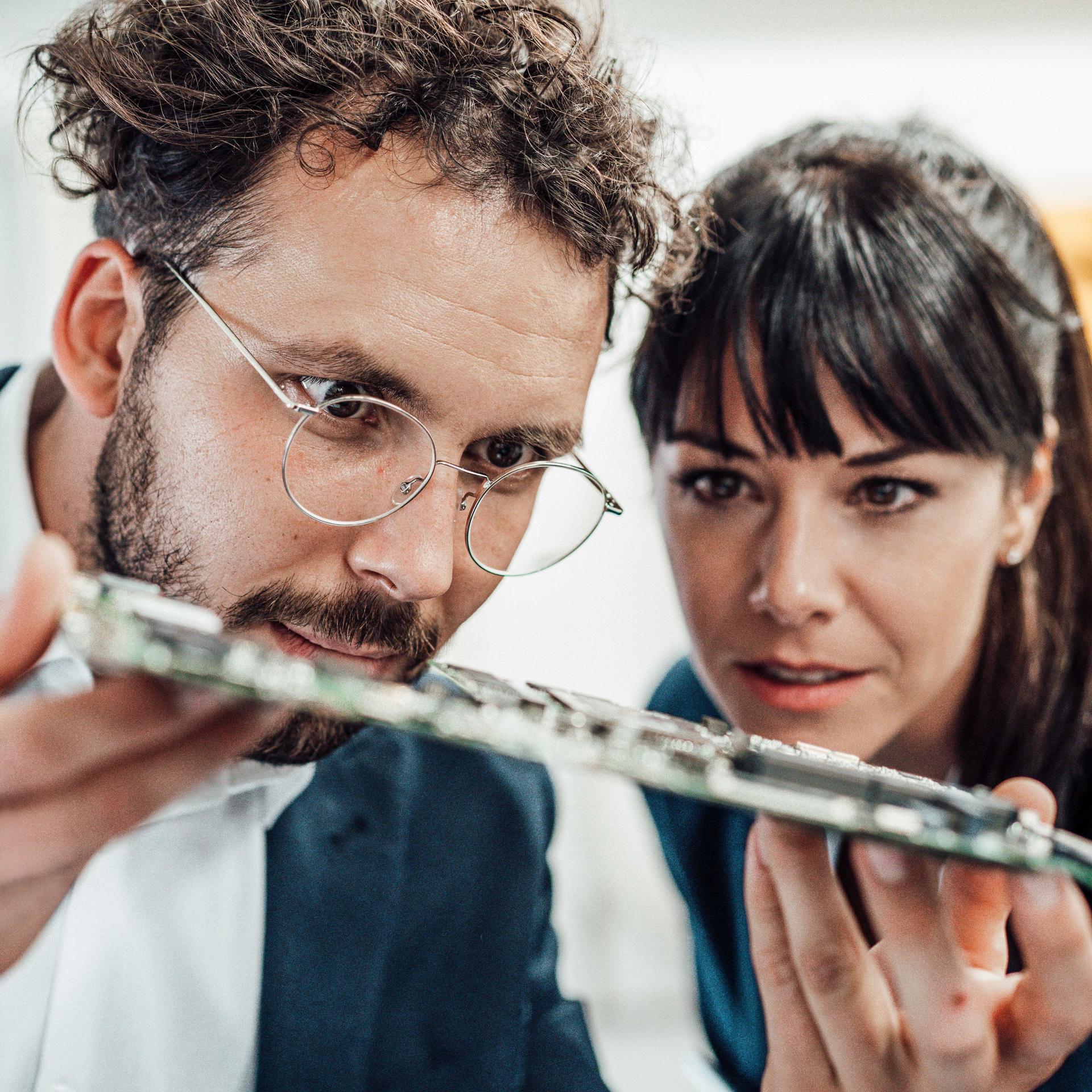 Ein Mann mit Brille und eine Frau untersuchen Leiterplatten in der Industrie.