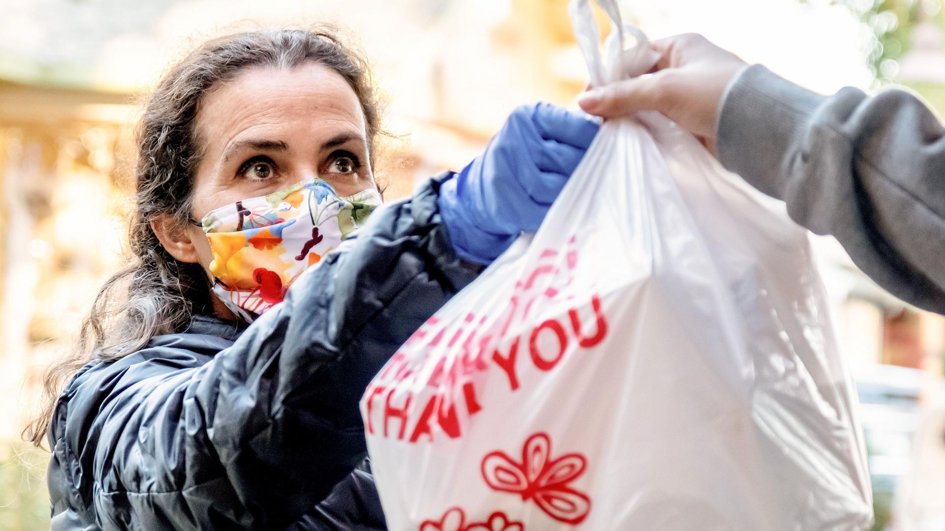 Eine Frau mit Mund-Nasen-Schutz nimmt eine Plastiktüte auf der "Thank you" steht entgegen.