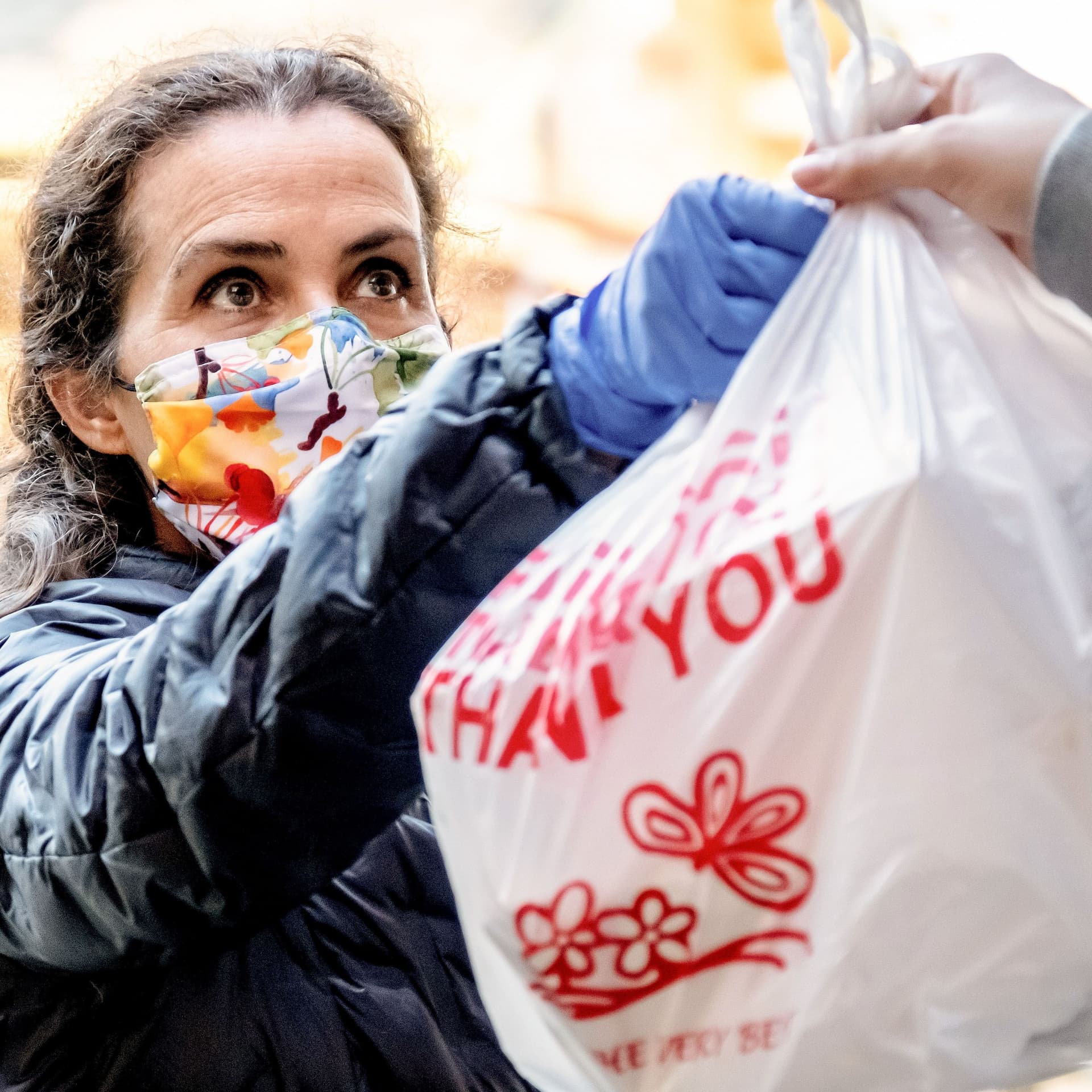 Eine Frau mit Mund-Nasen-Schutz nimmt eine Plastiktüte auf der "Thank you" steht entgegen.