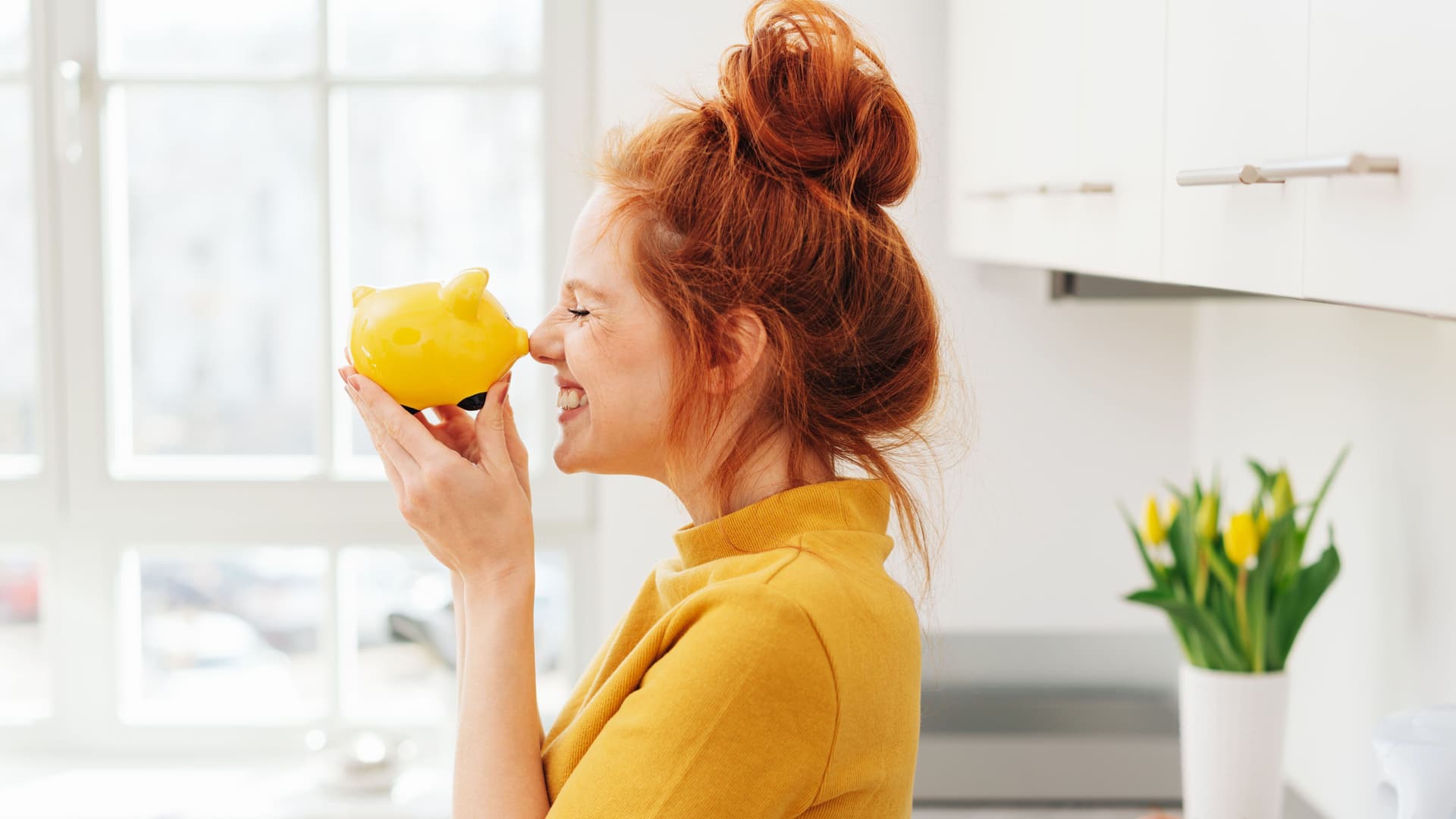 Eine Frau in gelbem Pullover hält ein gelbes Sparschwein an ihre Nase