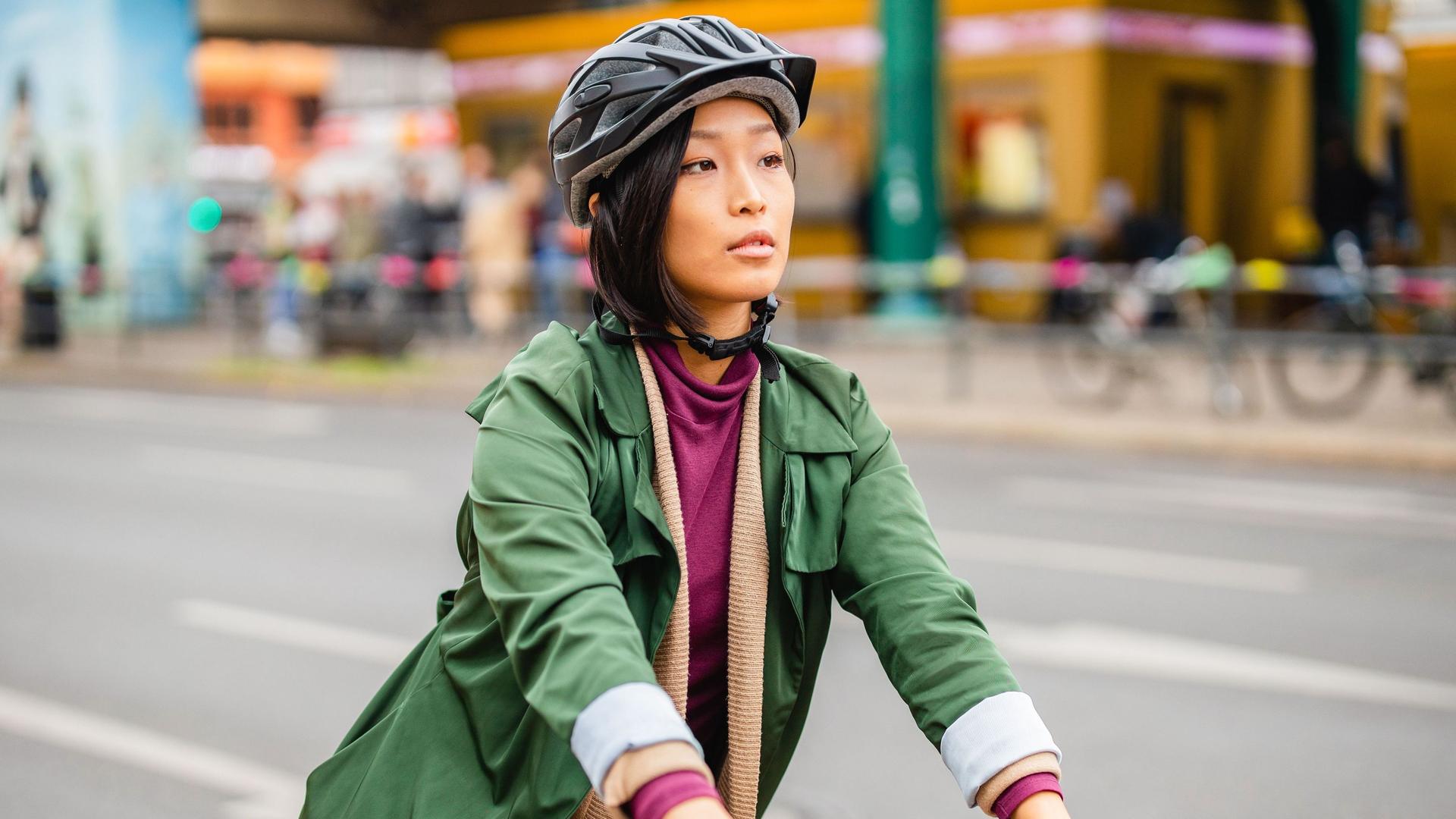 Eine Frau fährt in einer Großstadt Fahrrad. Sie trägt einen Fahrradhelm und elegante Kleidung.