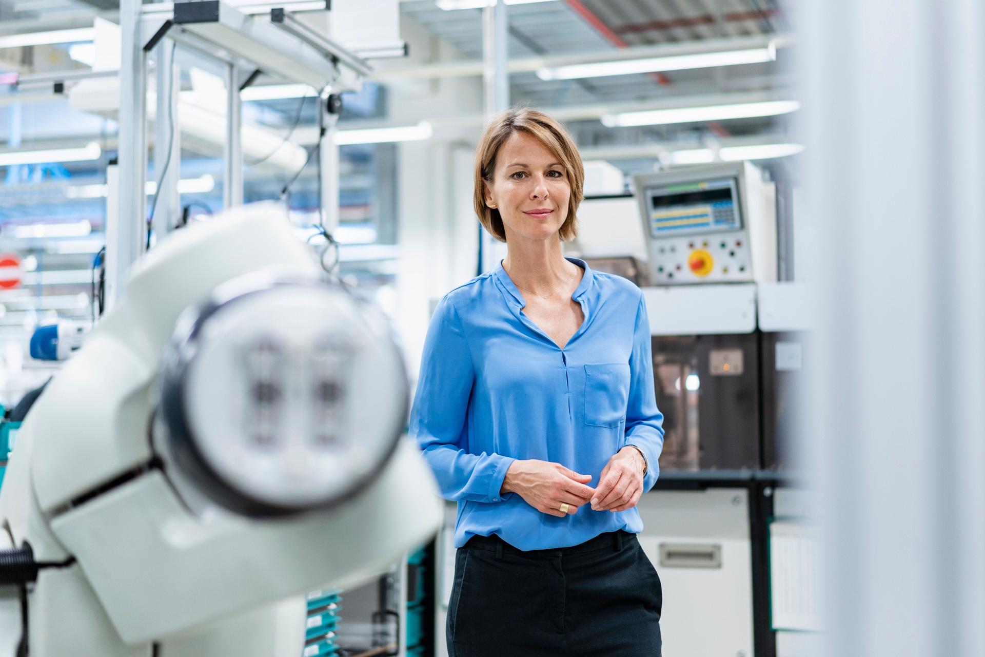 Porträt einer Frau am Montageroboter in einer Fabrik. Sie lächelt in die Kamera.