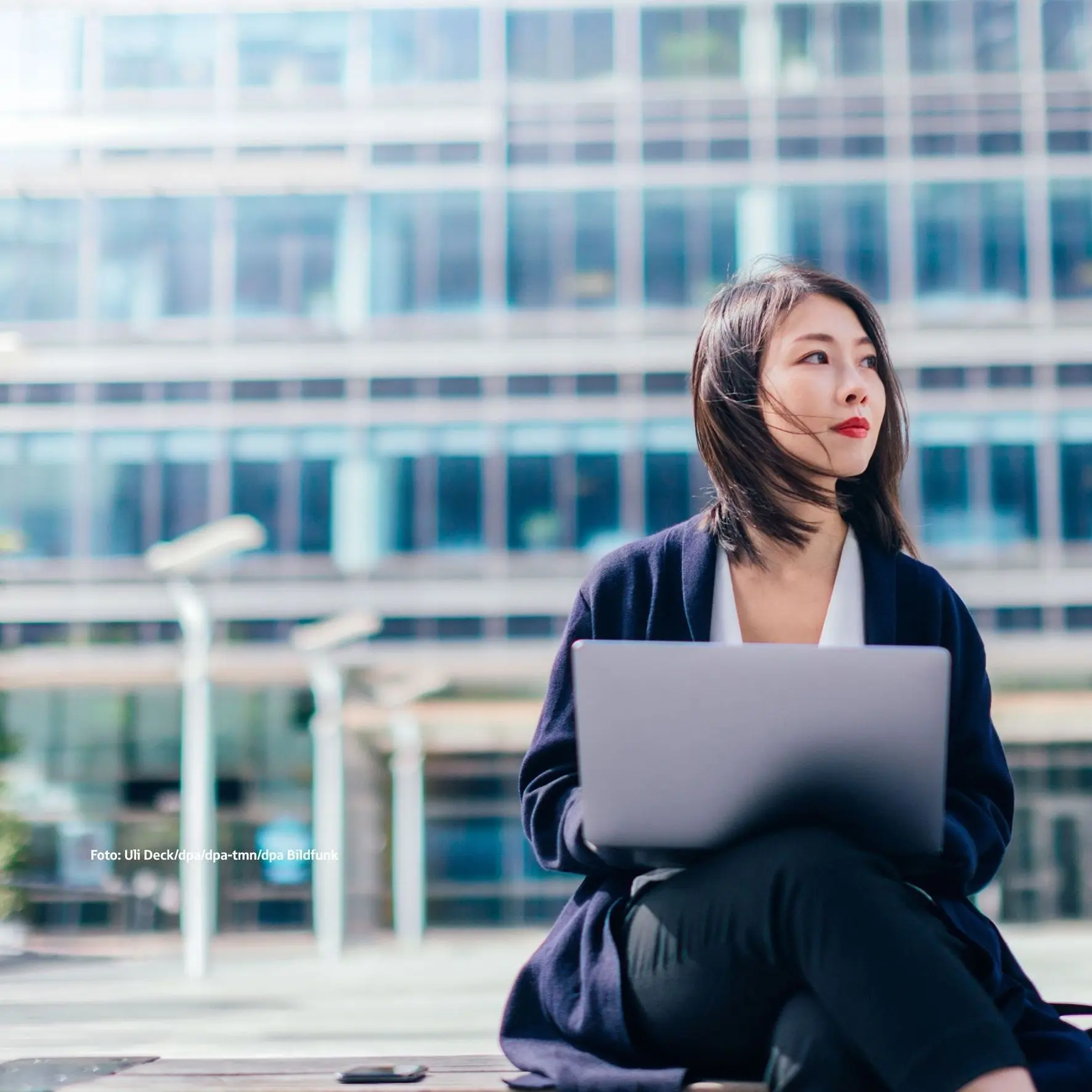 Frau sitzt mit Laptop draussen vor Bürogebäude