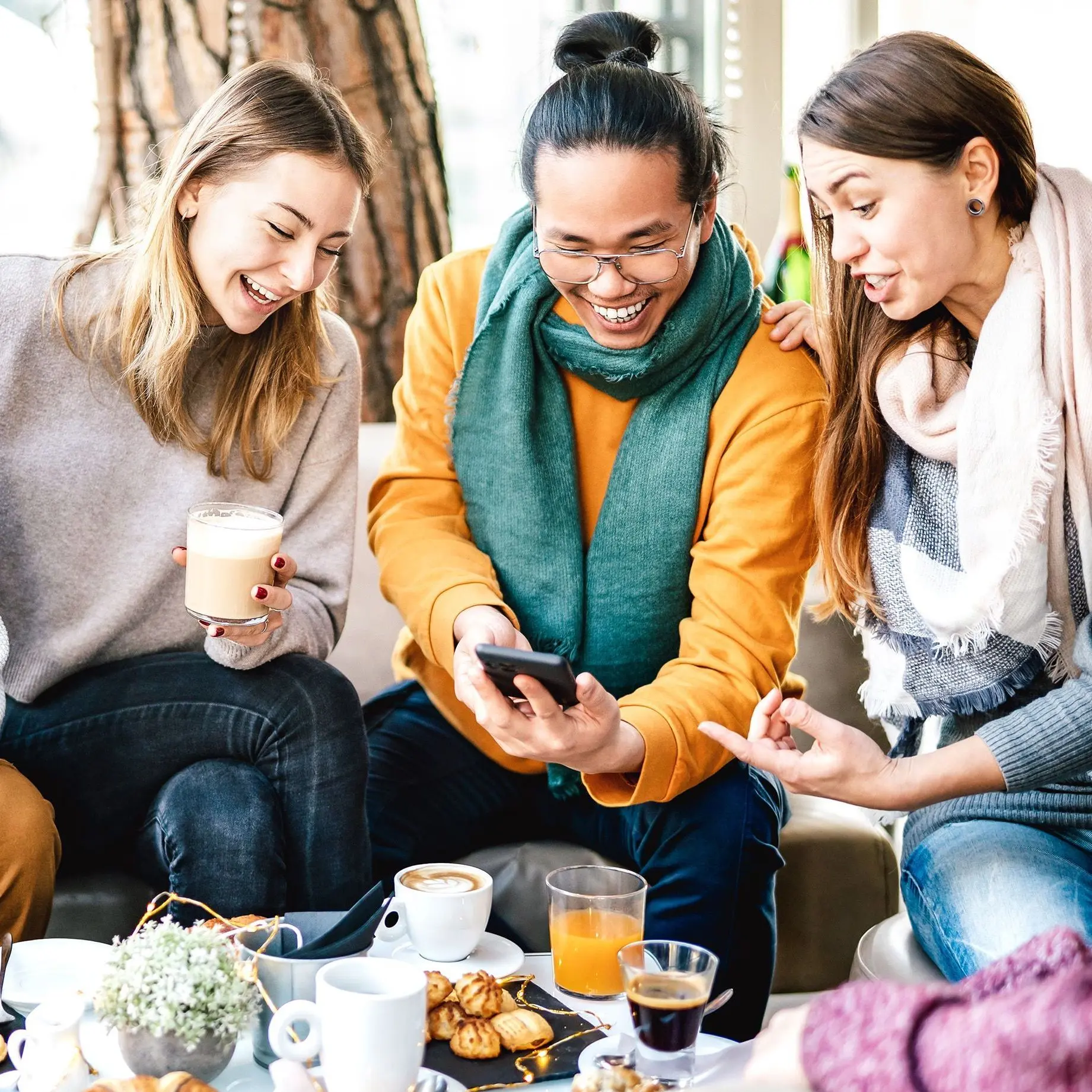 Freunde sitzen beim Essen und lachen. Einer hält ein Smartphone in der Hand.