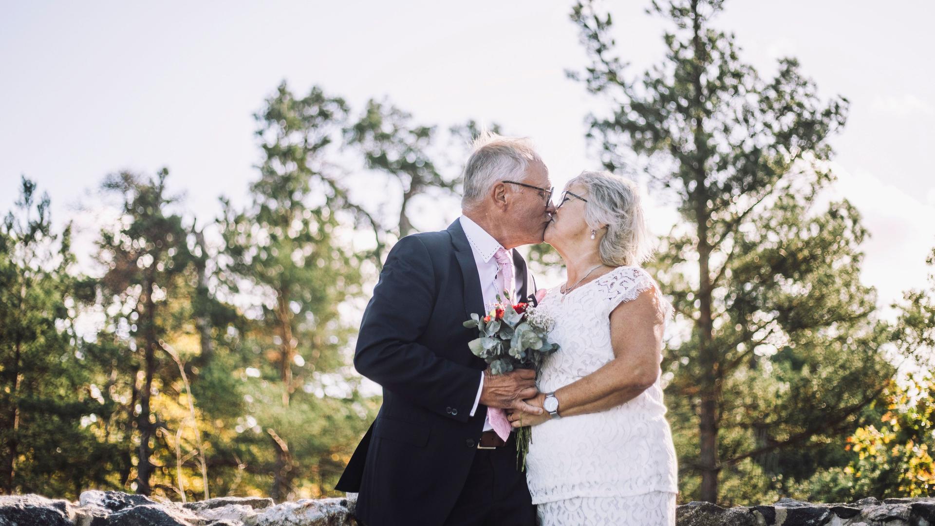 Liebevolles, frisch verheiratetes Seniorenpaar, das sich am Hochzeitstag vor dem Wald  küsst