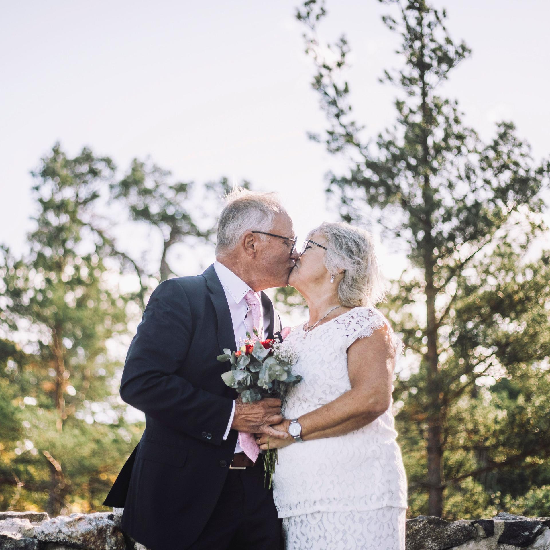 Liebevolles, frisch verheiratetes Seniorenpaar, das sich am Hochzeitstag vor dem Wald  küsst