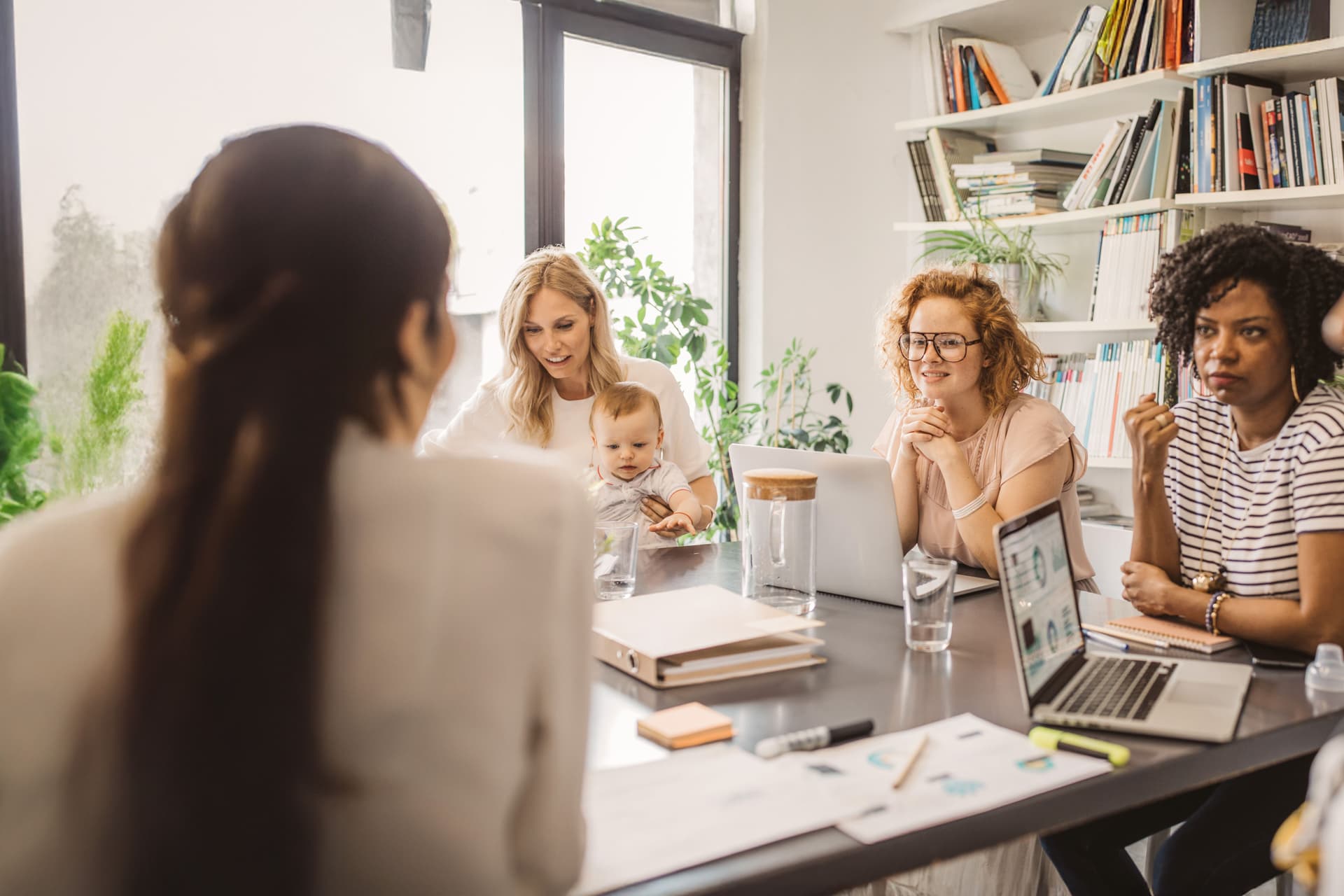 Fünf junge Frauen in einem Büromeeting, eine davon mit einem Baby auf dem Schoß.