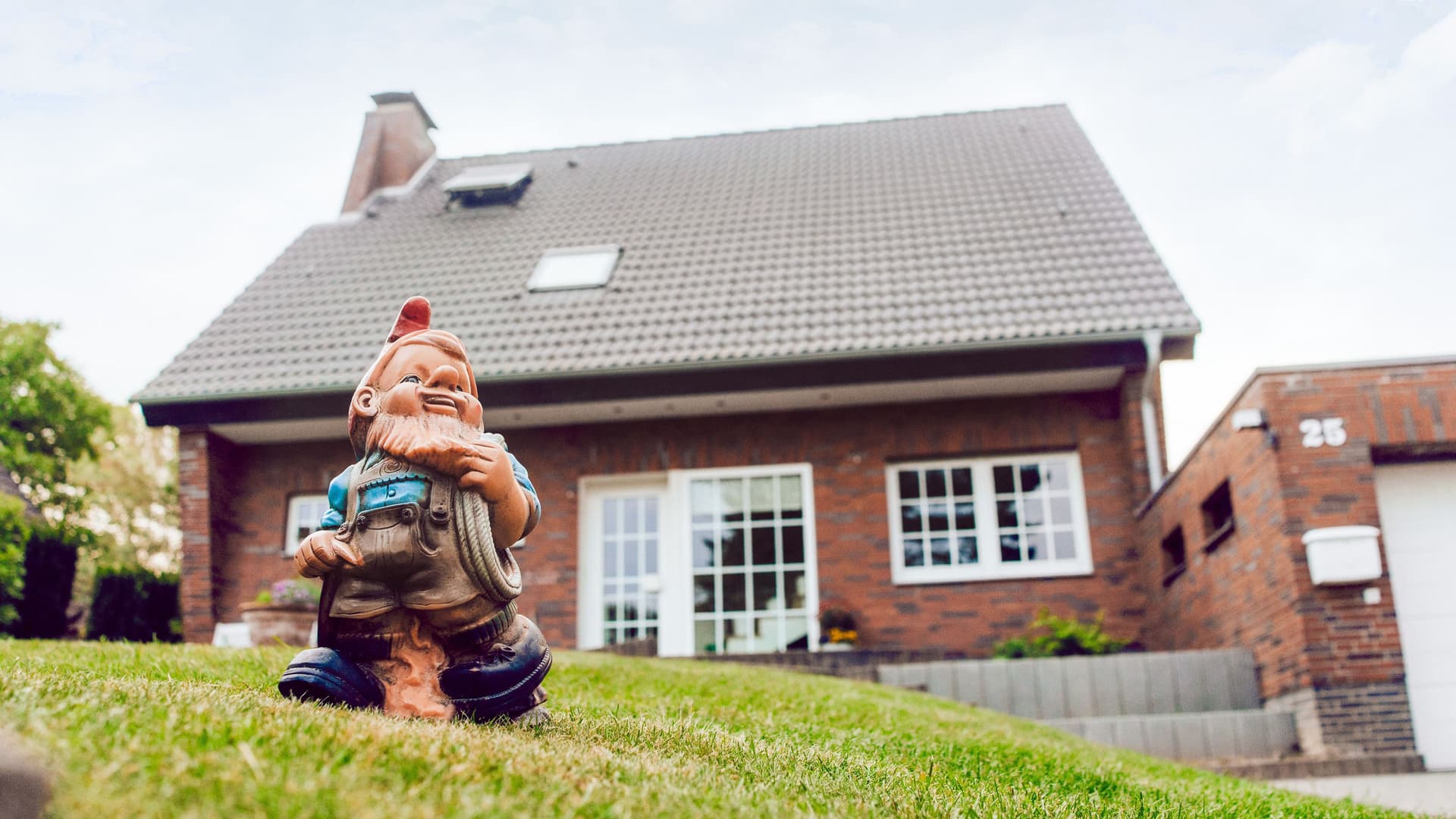 Aufnahme eines Gartenzwergs, der auf einer grünen Wiese vor einem Einfamilienhaus steht.