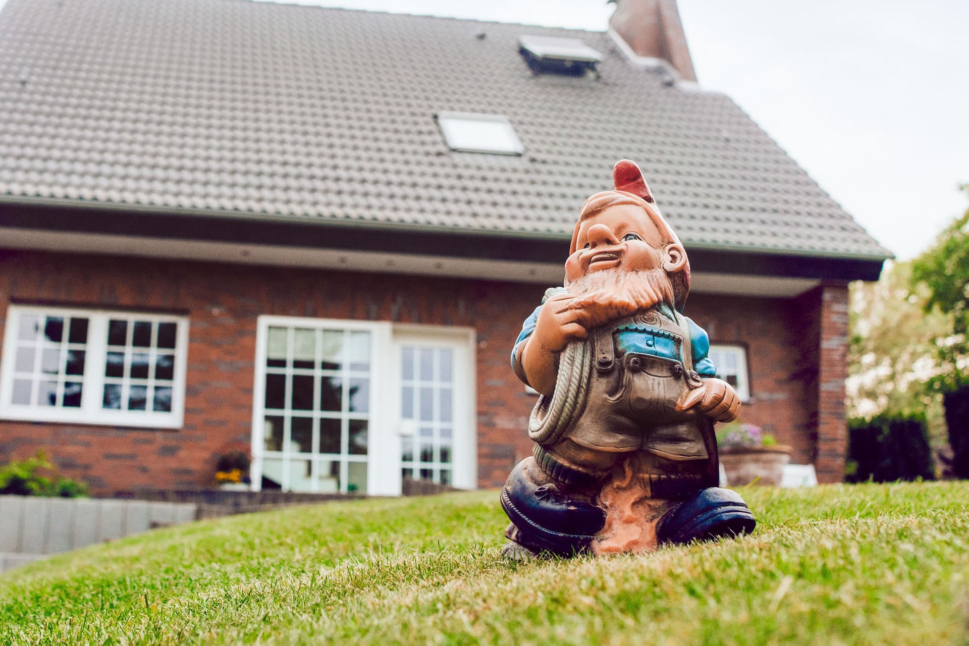 Aufnahme eines Gartenzwergs, der auf einer grünen Wiese vor einem Einfamilienhaus steht.