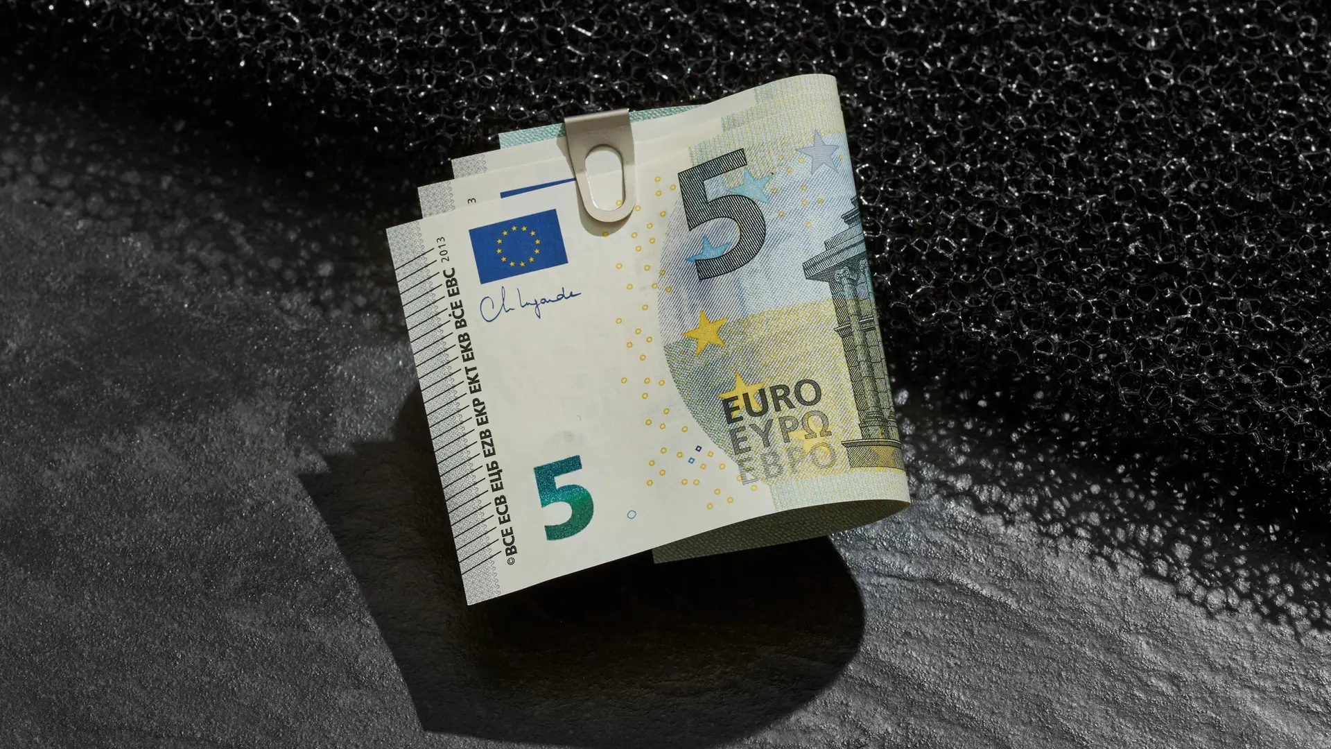 Ein Buendel 5-Euroscheine mit einer klammer befestigt liegt auf einer Kante.