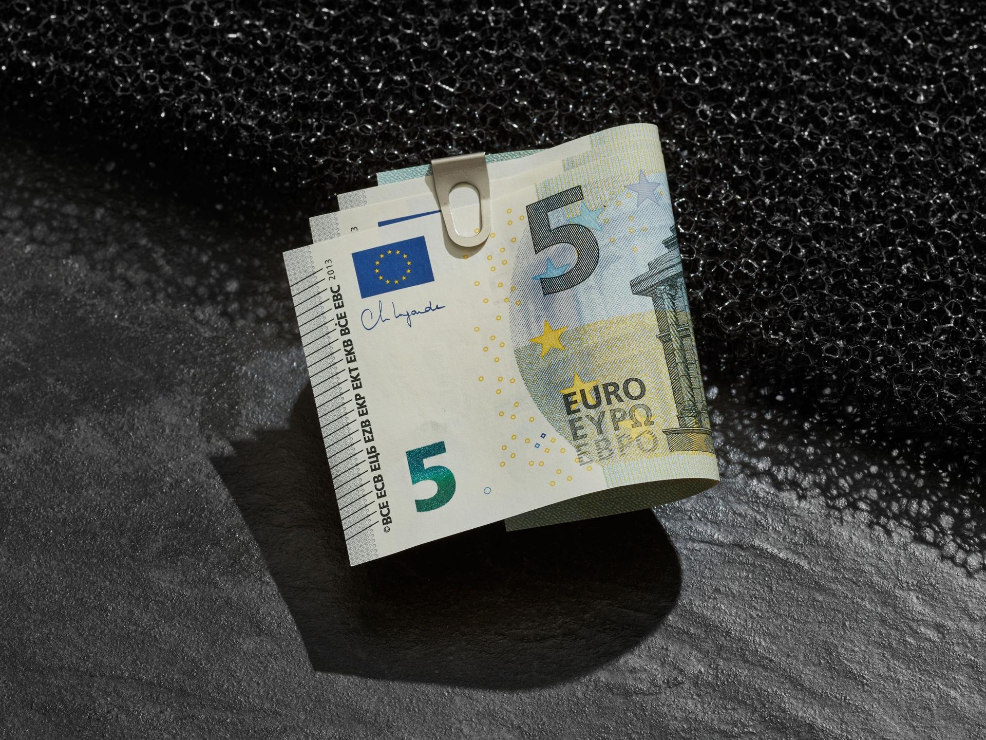 Ein Buendel 5-Euroscheine mit einer klammer befestigt liegt auf einer Kante.