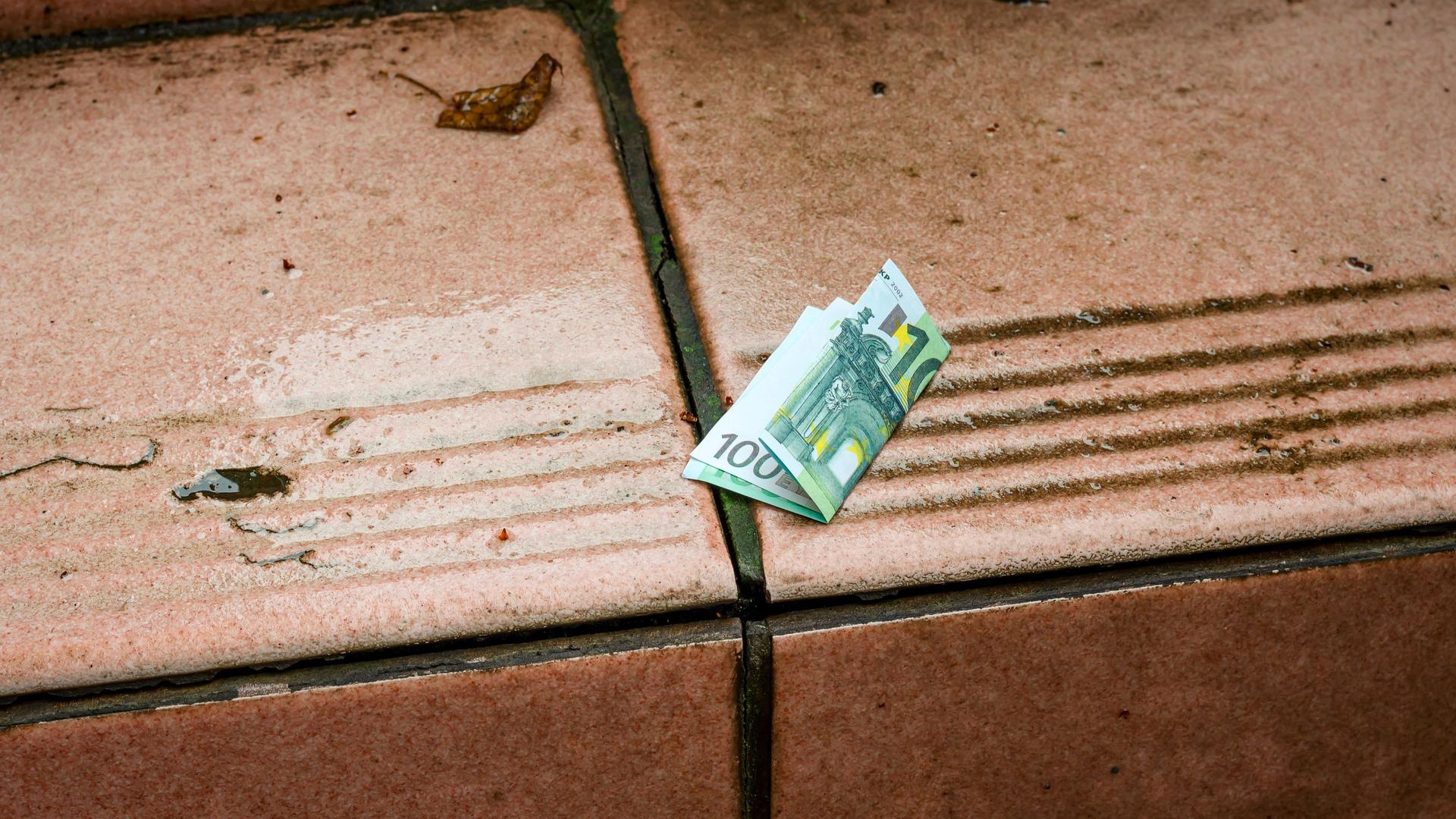 Ein 100-Euro-Schein liegt gefaltet auf einer nassen Treppe.