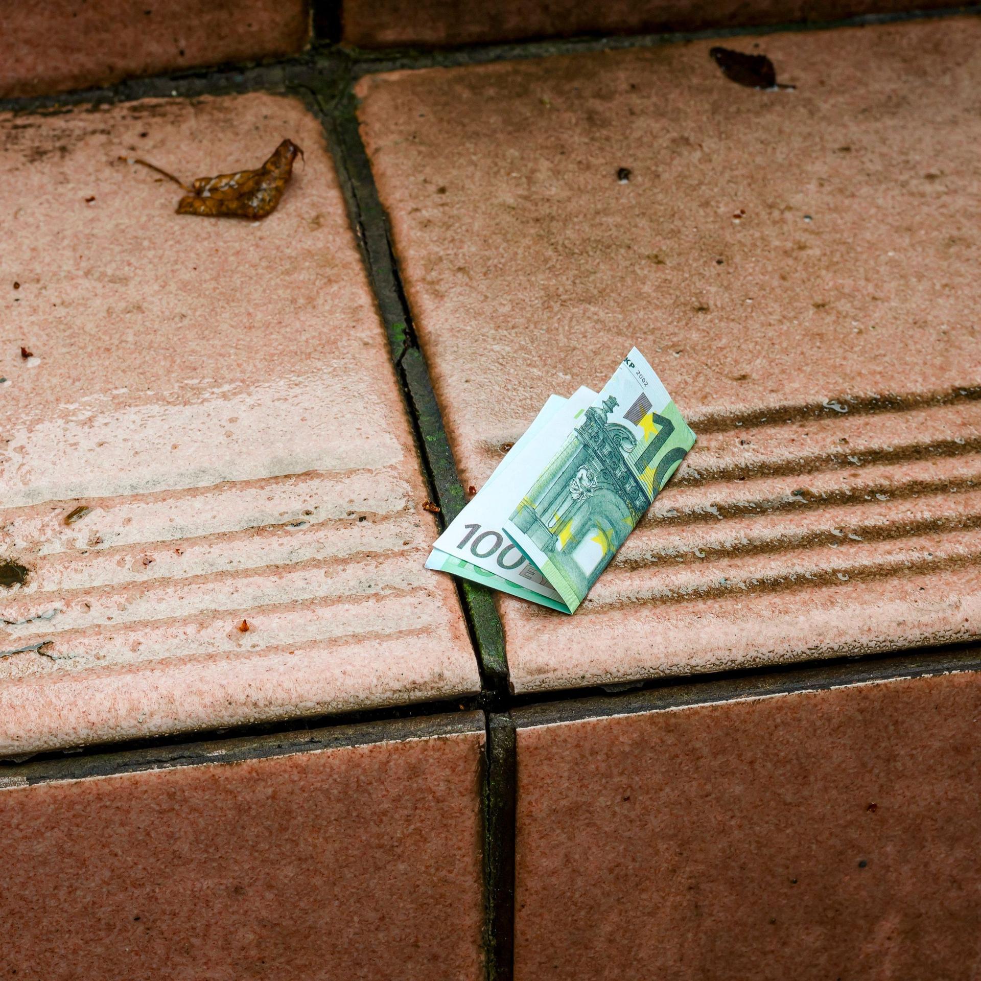 Ein 100-Euro-Schein liegt gefaltet auf einer nassen Treppe.