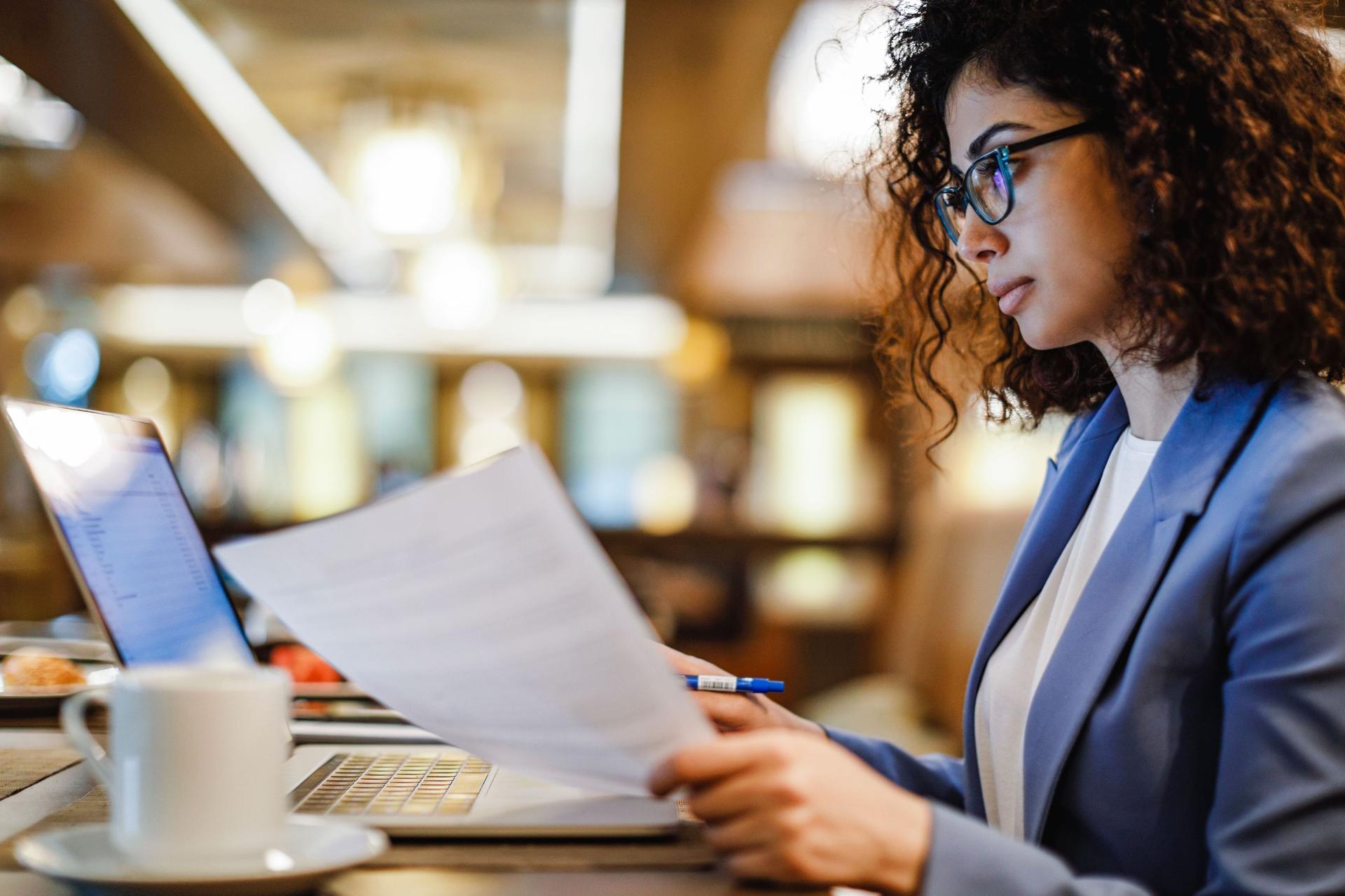 Eine Frau in Business-Kleidung sitzt in einem Café und arbeitet mit ihrem Laptop.