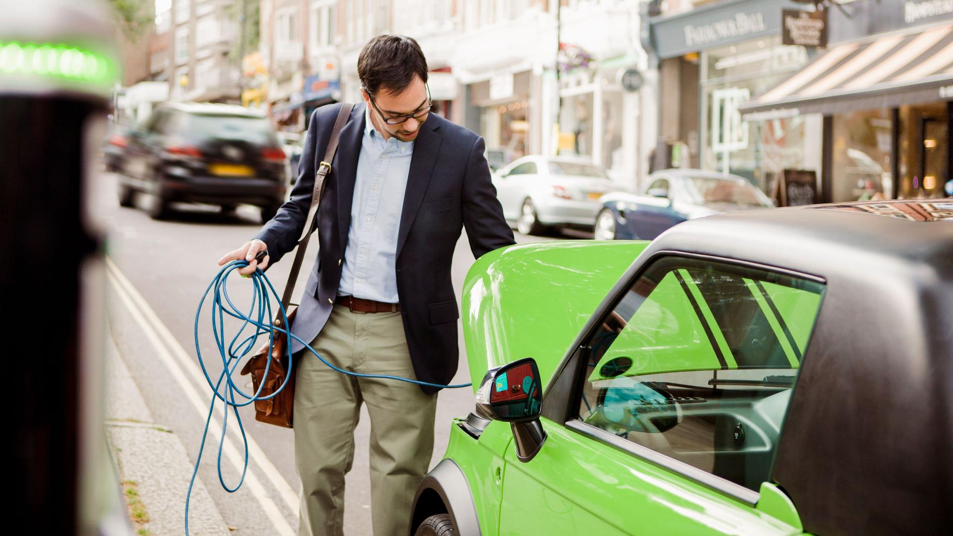 Mann im Anzug lädt ein auffällig grün lackiertes Elektroauto auf.