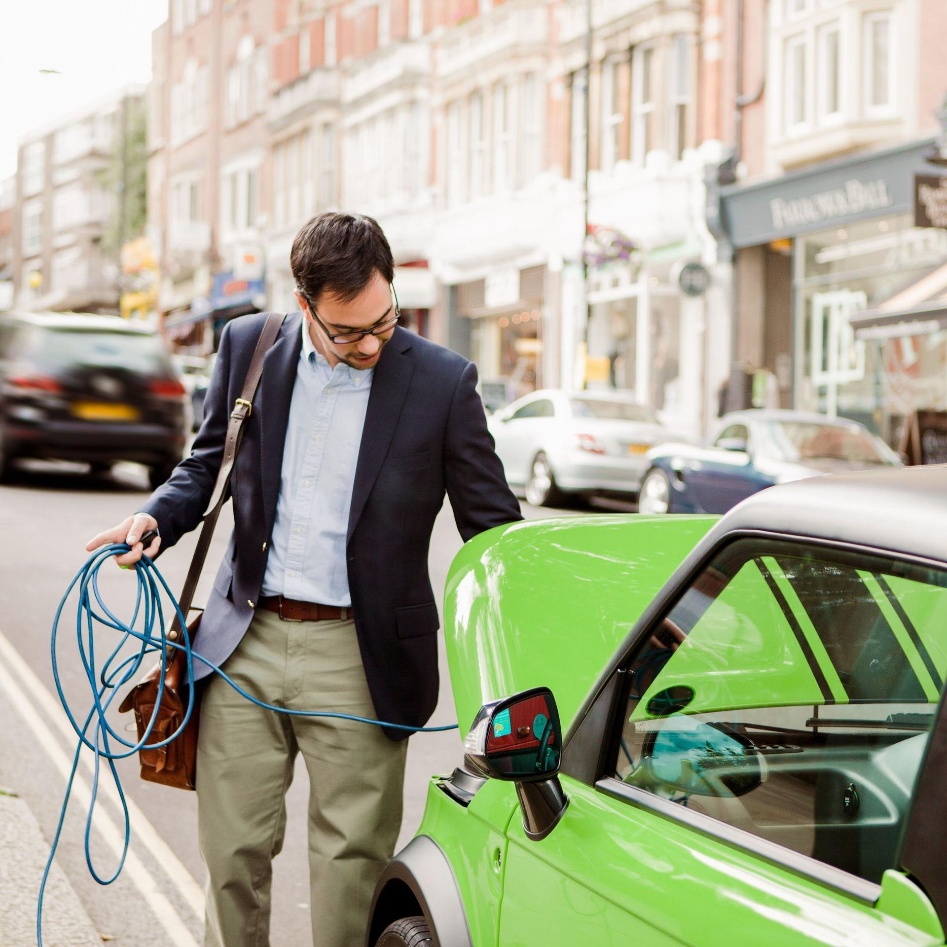 Mann im Anzug lädt ein auffällig grün lackiertes Elektroauto auf.