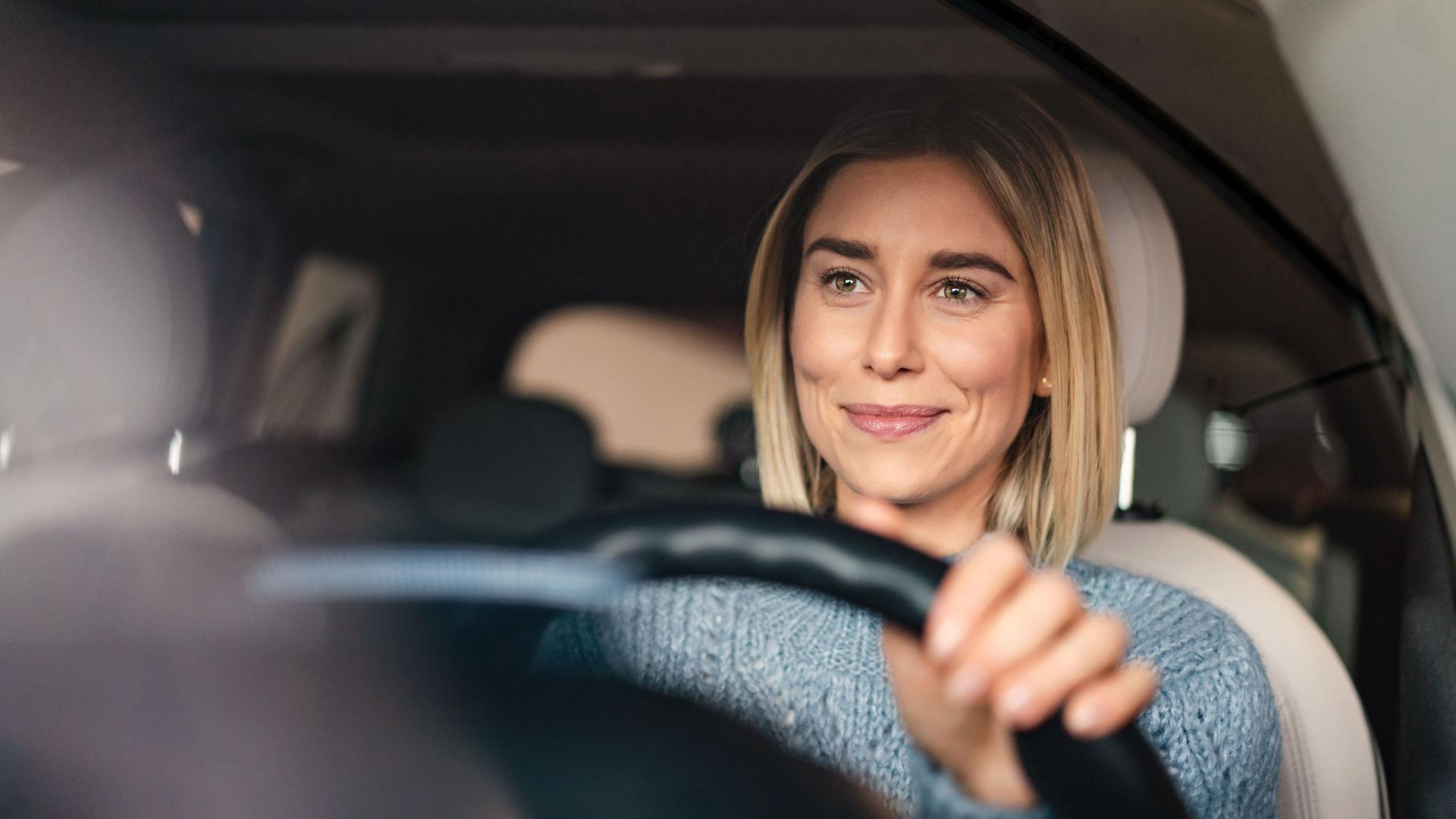 Porträt einer lächelnden Frau hinter dem Steuer ihres Autos.