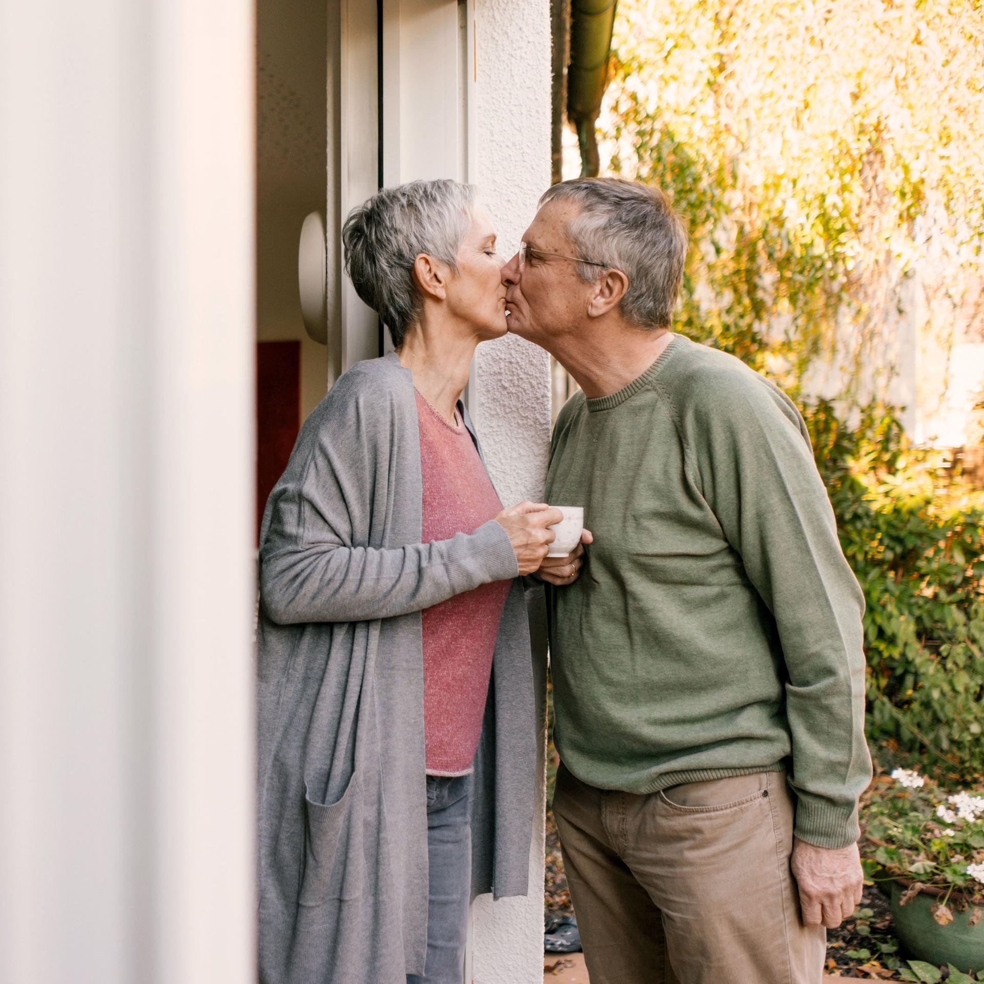 Älteres Paar küsst sich an einer Terrassentür.