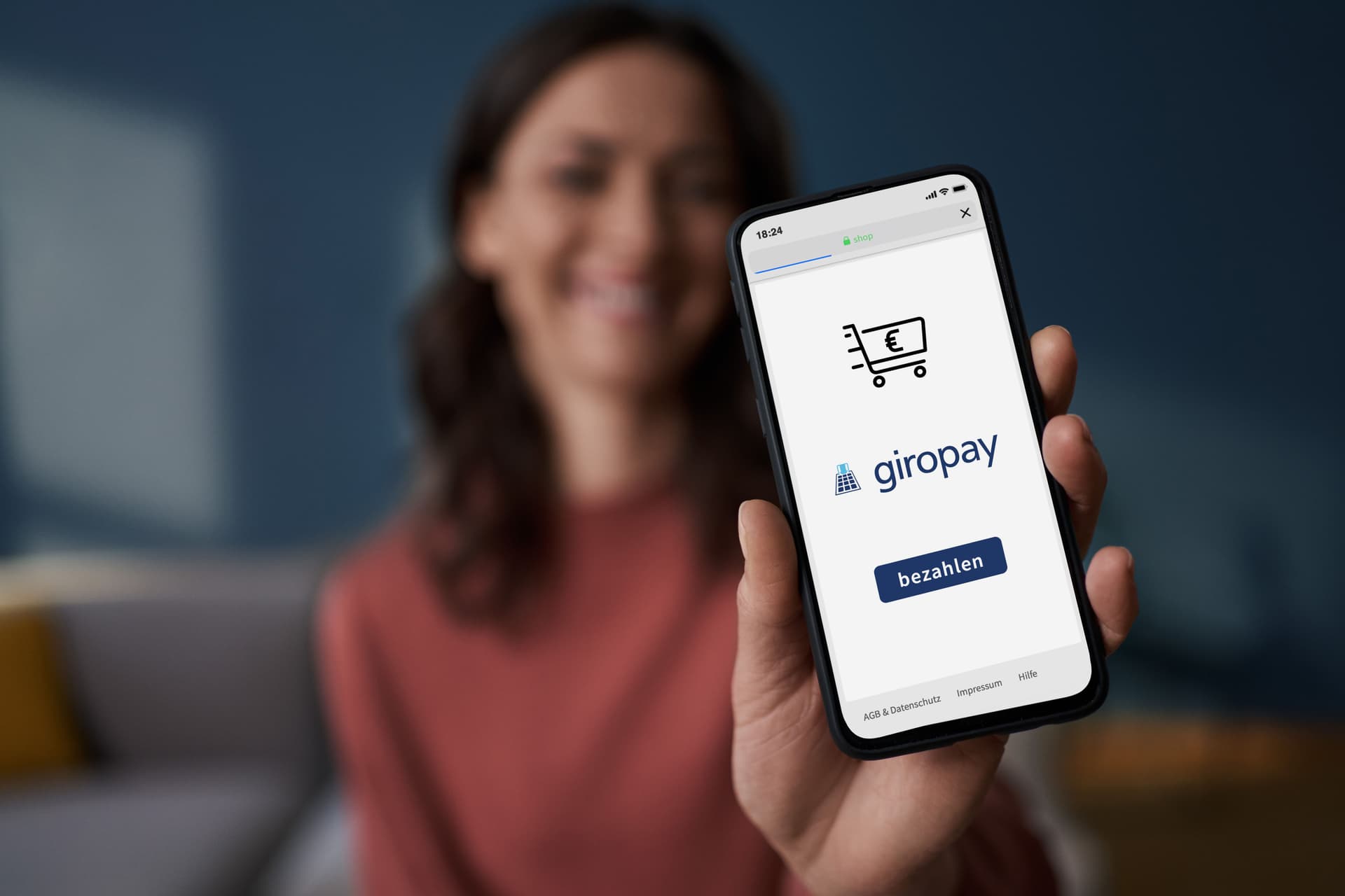 Frau, auf einen Sofa sitzend, hält Handy mit Giropay App vor die Kamera