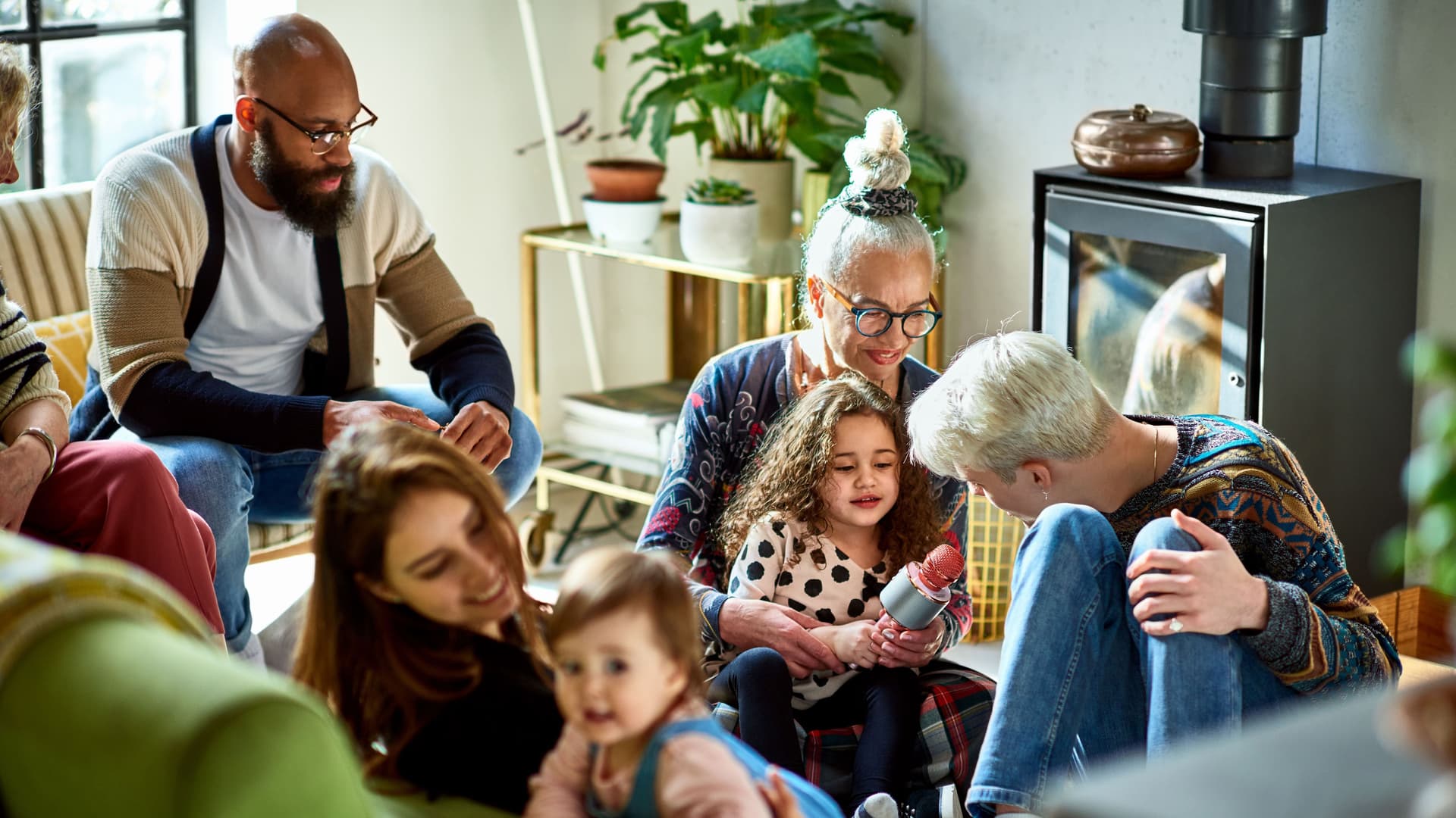 Große Familie sitzt im Wohnzimmer auf Couch und Boden und spielt mit den Kindern