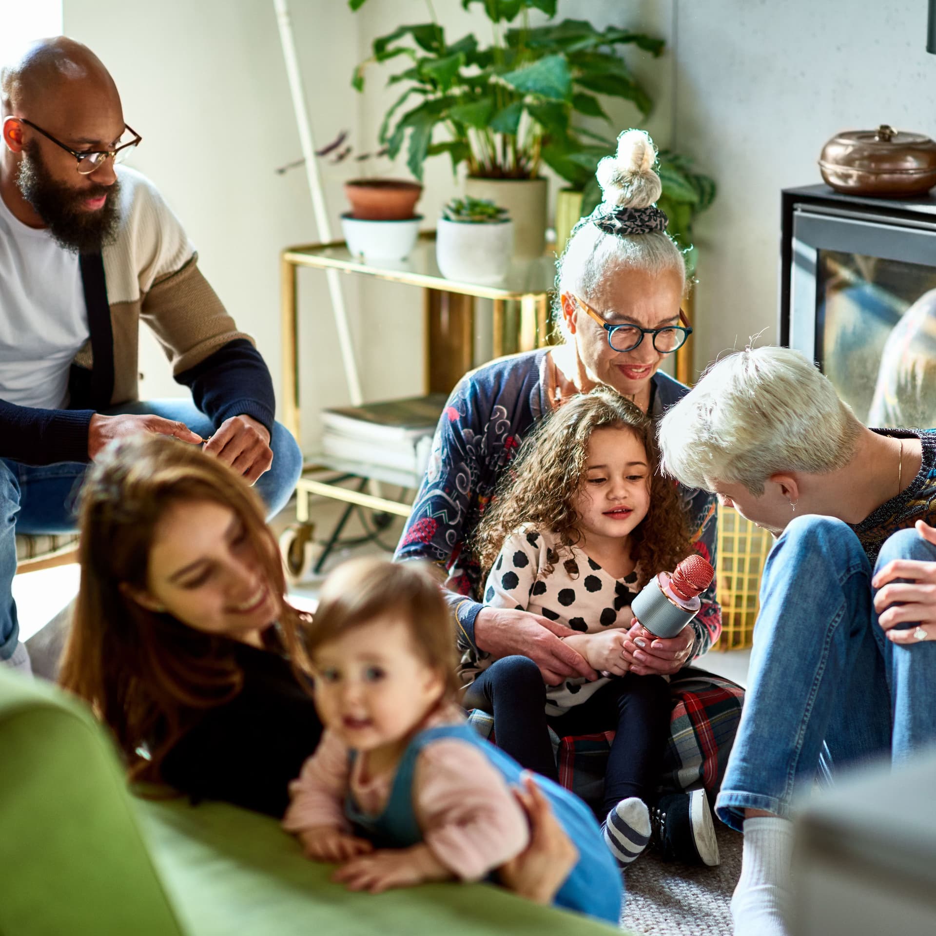 Große Familie sitzt im Wohnzimmer auf Couch und Boden und spielt mit den Kindern