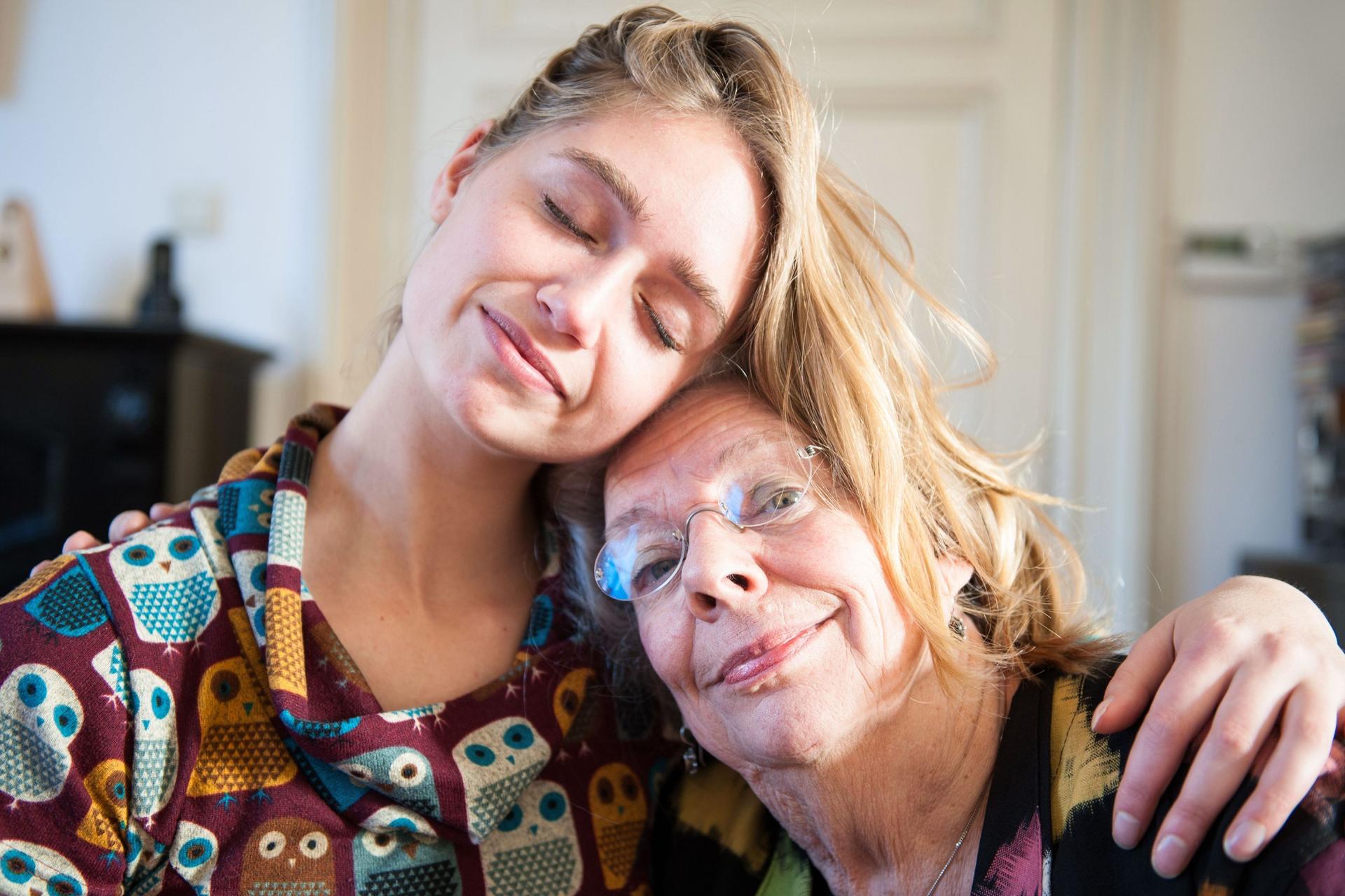 Großmutter und erwachsene Enkelin umarmen sich und lehnen die Köpfe aneinander.
