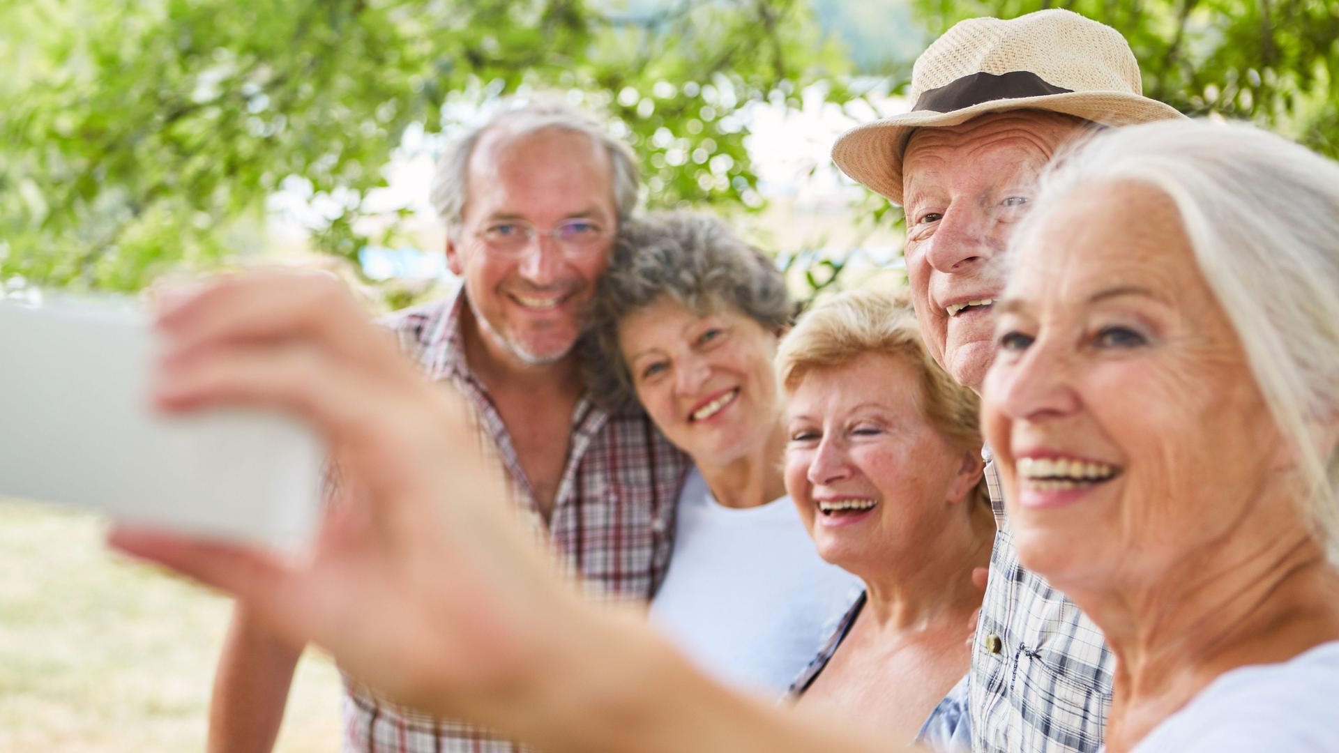 Ältere Frau macht von sich und ihren vier Freunden ein Selfie. Alle lächeln bei sommerlichen Temperaturen in die Kamera.,