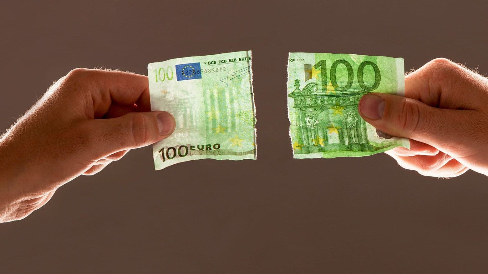 Zwei Hände halten jeweils eine Hälfte eines zerissenen hundert-Euro-Scheines in die Luft. Im Gegenlicht sind die Wasserzeichen zu erkennen.