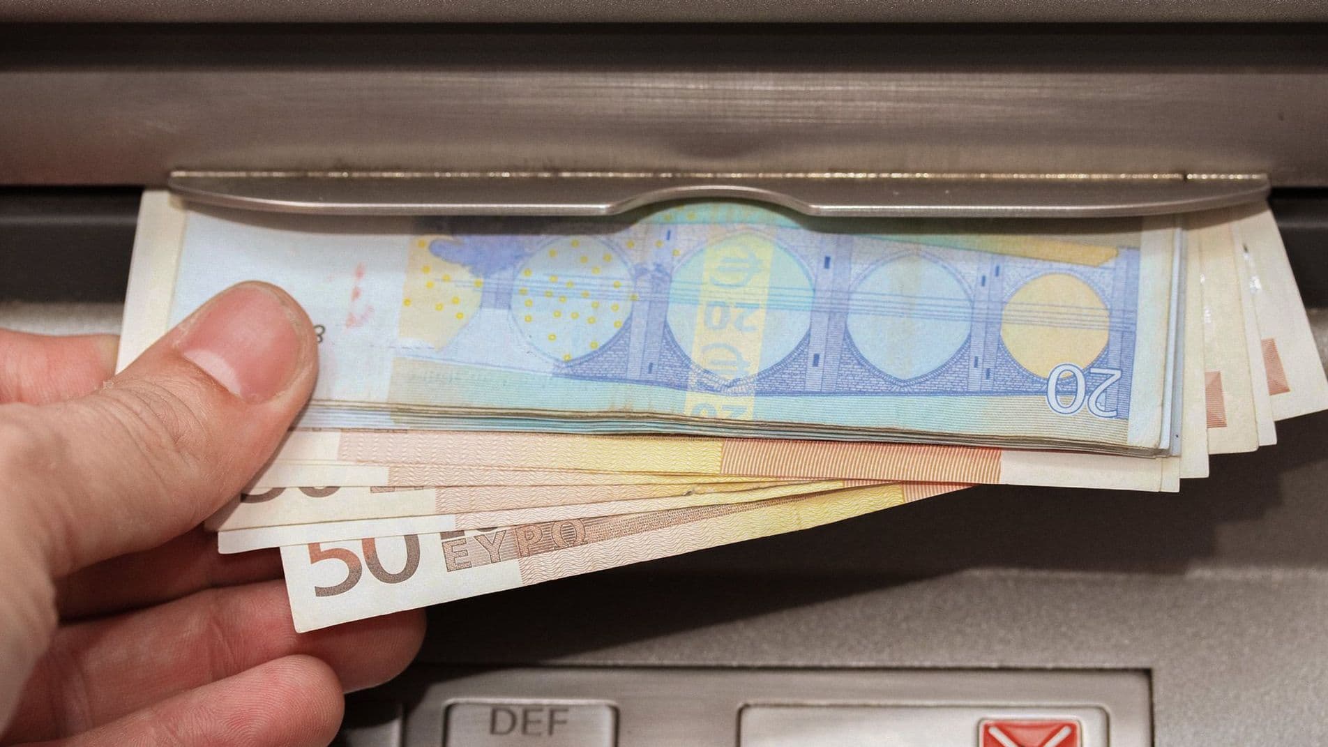 Nahaufnahme einer Hand die verschiedene Euro-Banknoten aus einem Bankautomaten entnimmt.