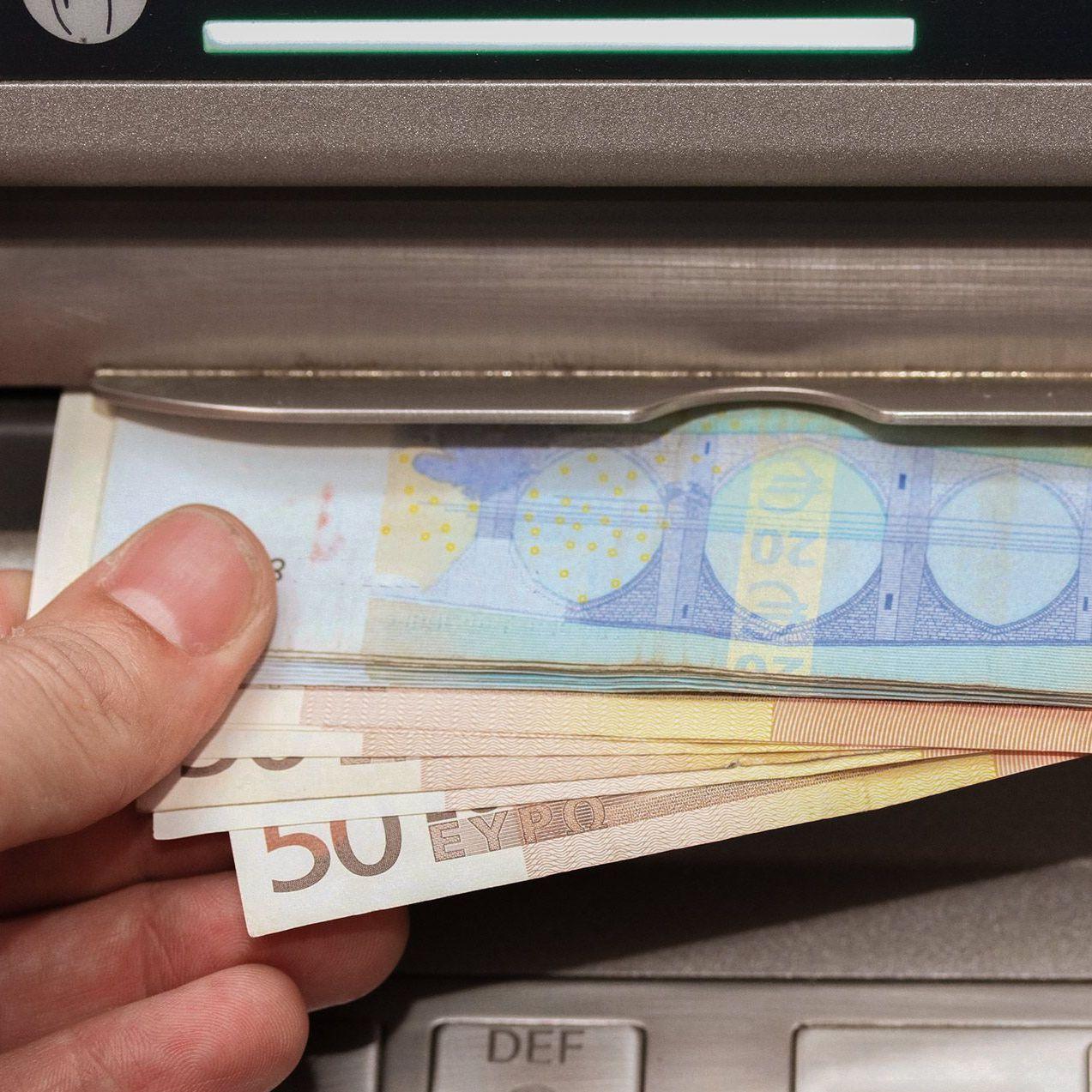 Nahaufnahme einer Hand die verschiedene Euro-Banknoten aus einem Bankautomaten entnimmt.