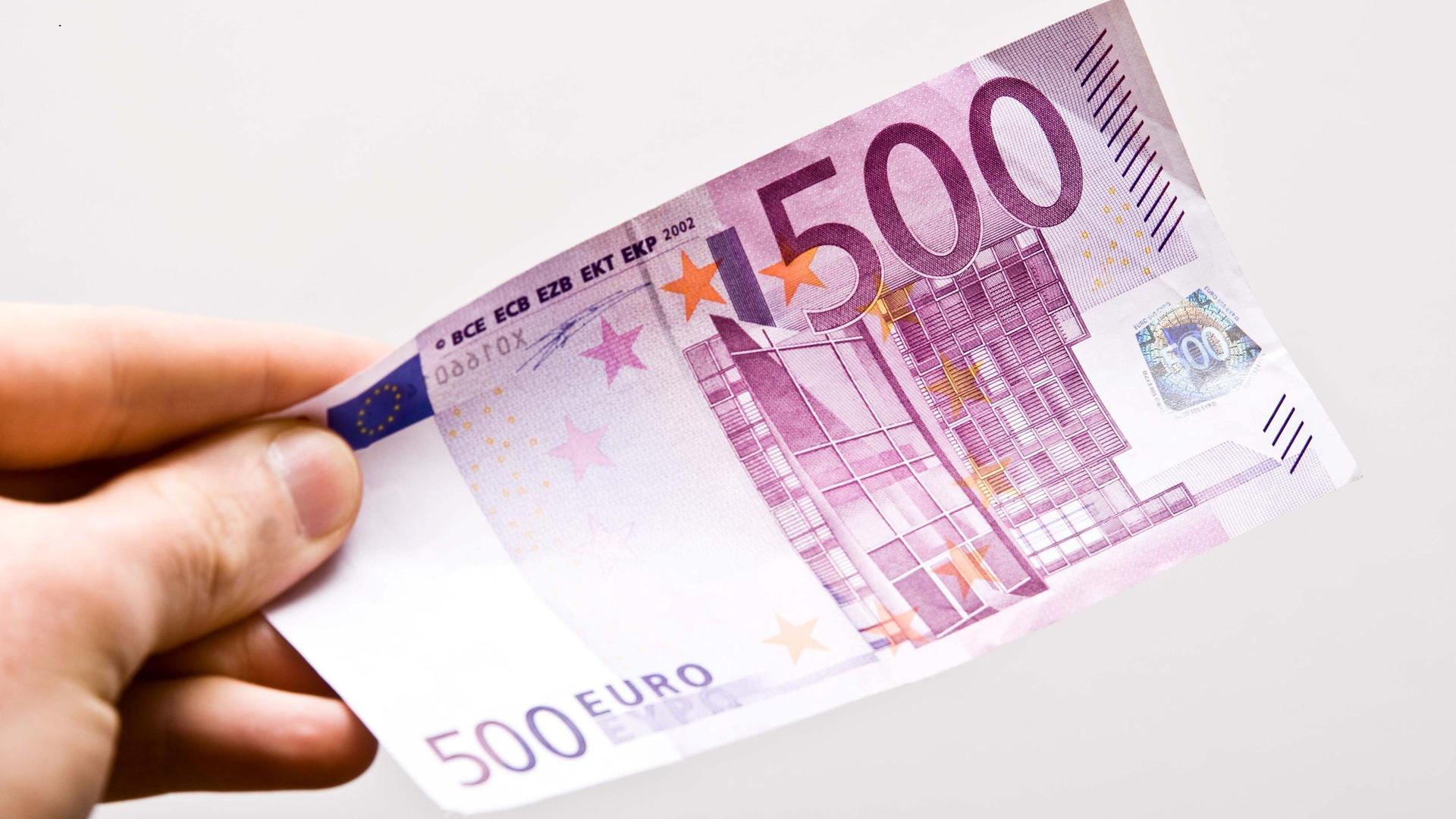 Nahaufnahme einer Hand, die einen fünfhundert-Euro-Schein hochhält. Der Hintergrund ist weiß.