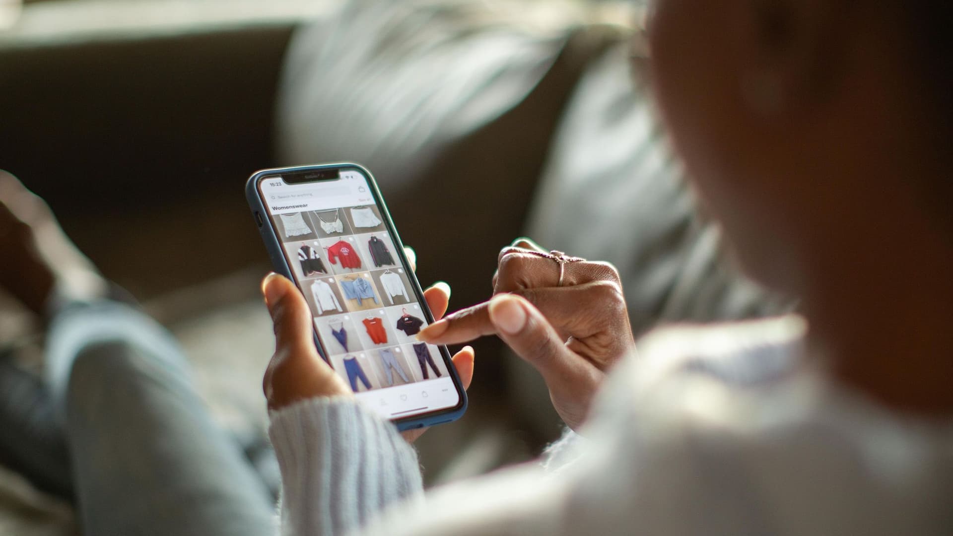 Schulterblick auf eine Hand mit Smartphone. Auf dem Smartphone sieht man die Seite eines Onlineshops.