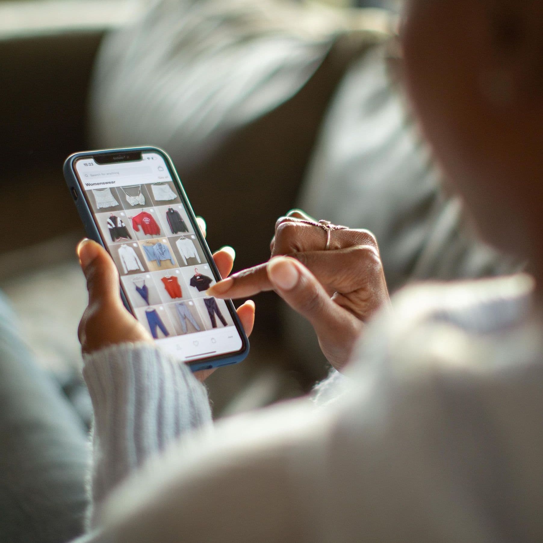 Schulterblick auf eine Hand mit Smartphone. Auf dem Smartphone sieht man die Seite eines Onlineshops.