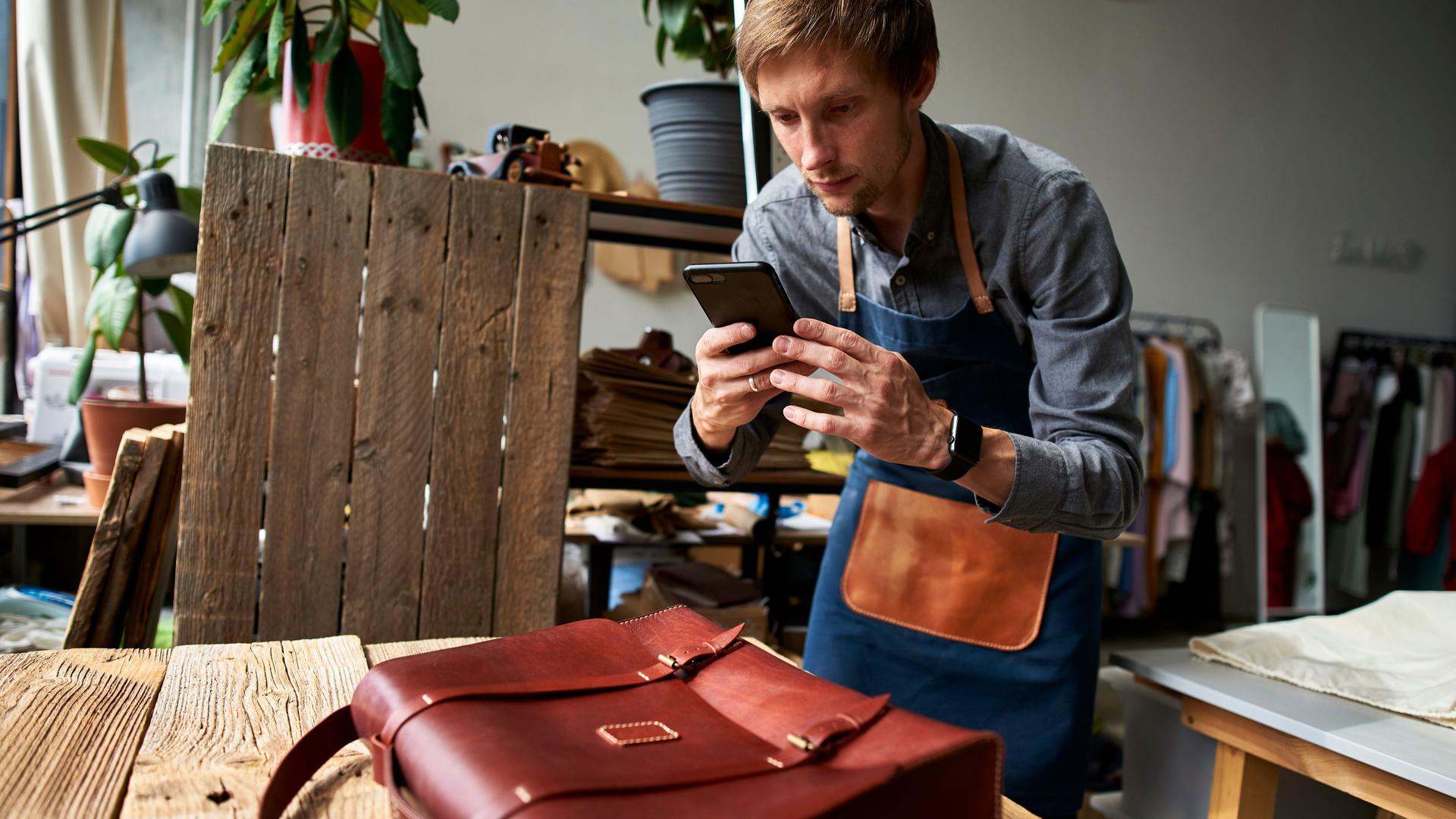 Ein Handwerker macht in seiner Werkstatt ein Handyfoto von einer braunen Ledertasche.