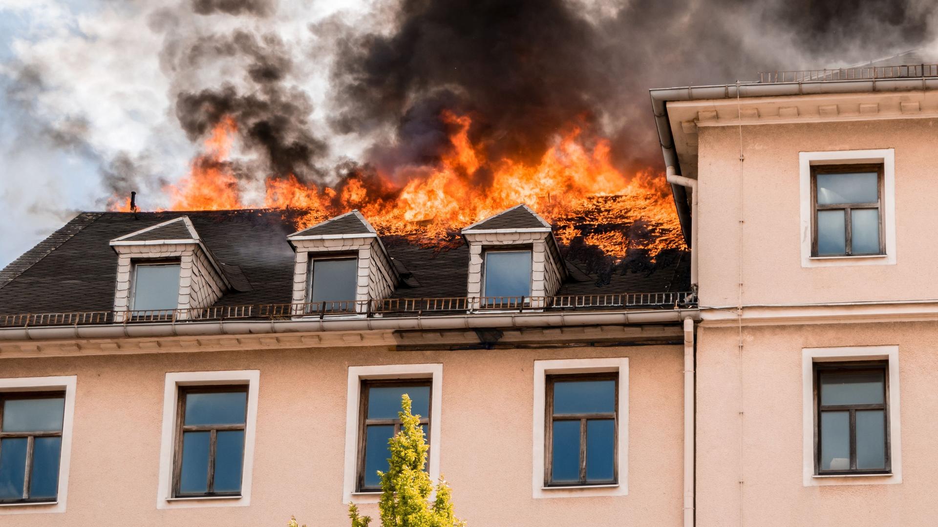 Dachstuhl von lachsfarbenem Haus steht in Flammen. Rauch steigt auf.