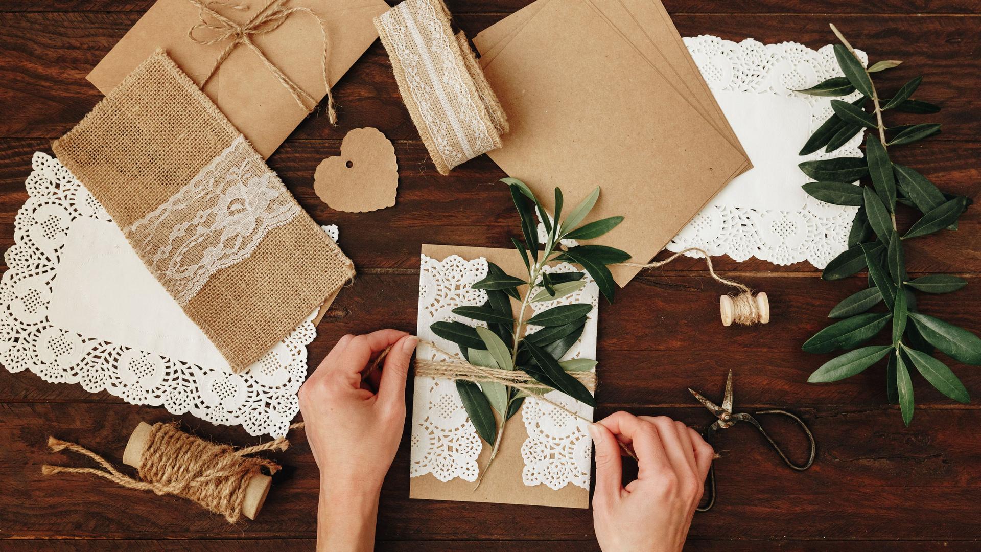 Hände binden Hochzeitseinladungen mit einem Pflanzenzweig auf einem Holztisch