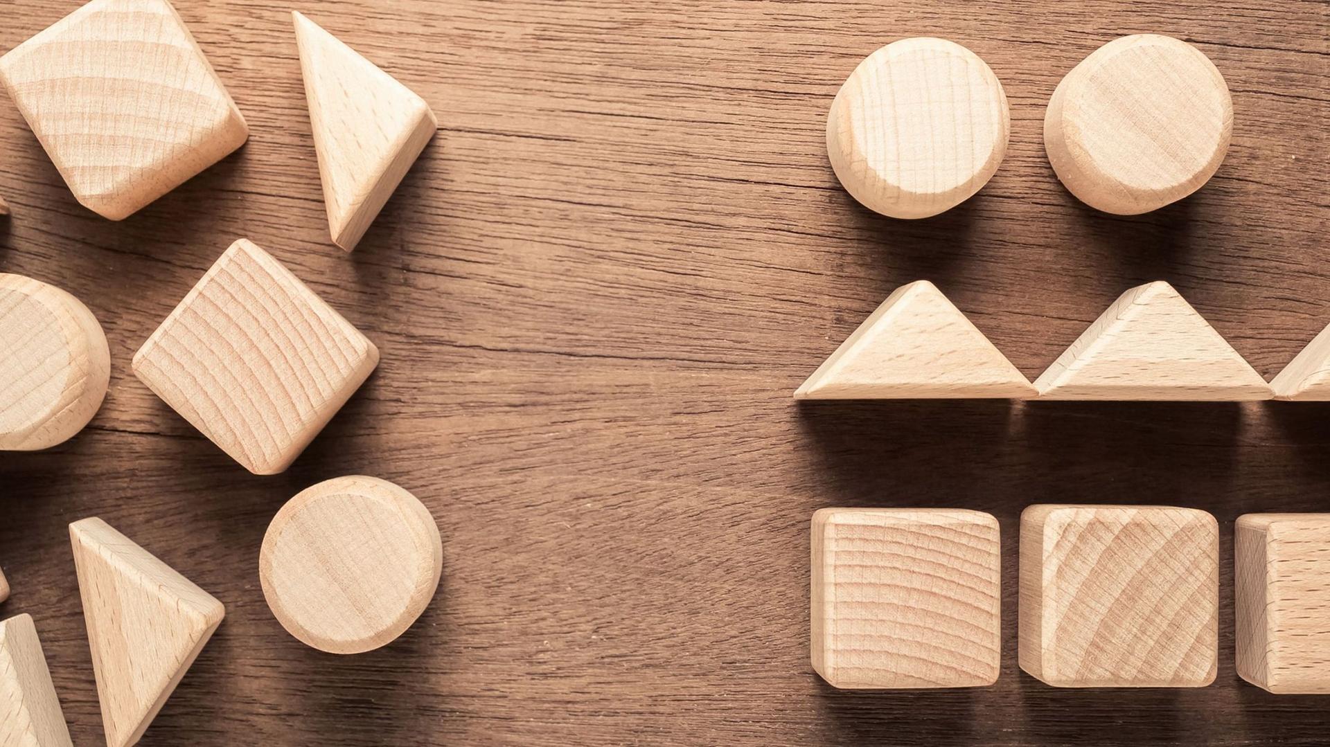 Auf einem Holztisch liegen sortierte und unsortierte Holzklötze in verschiedene geometrischen Formen.