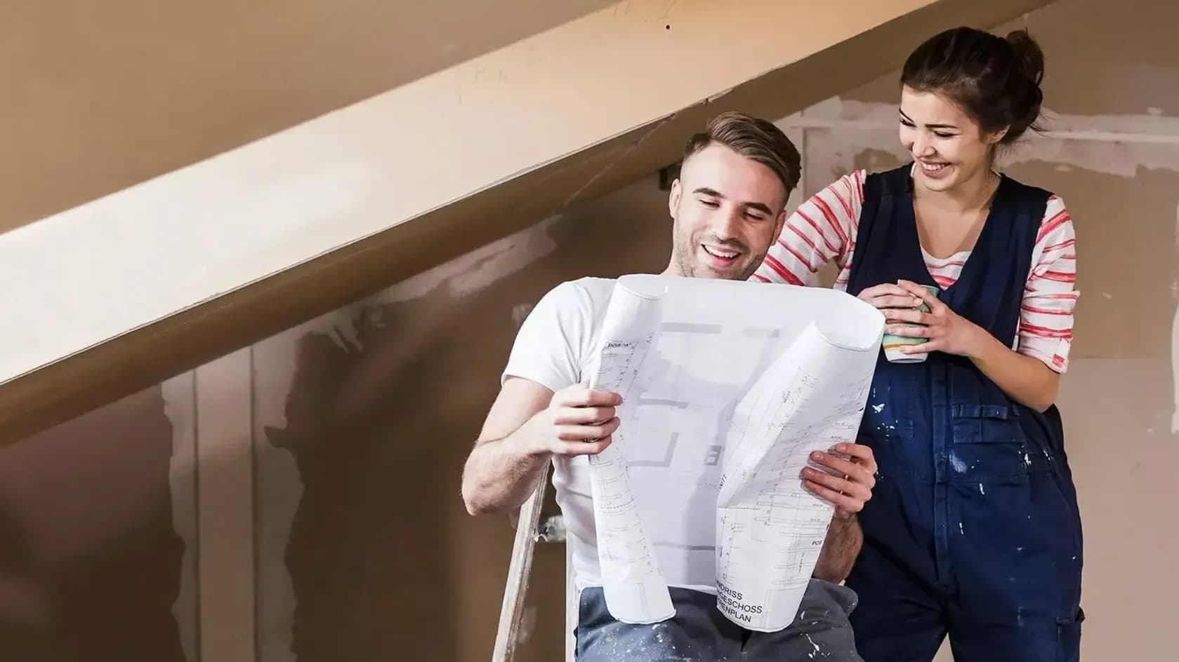 ein junges Paar in einem unrenovierten Dachgeschoss guckt auf einen Bauplan