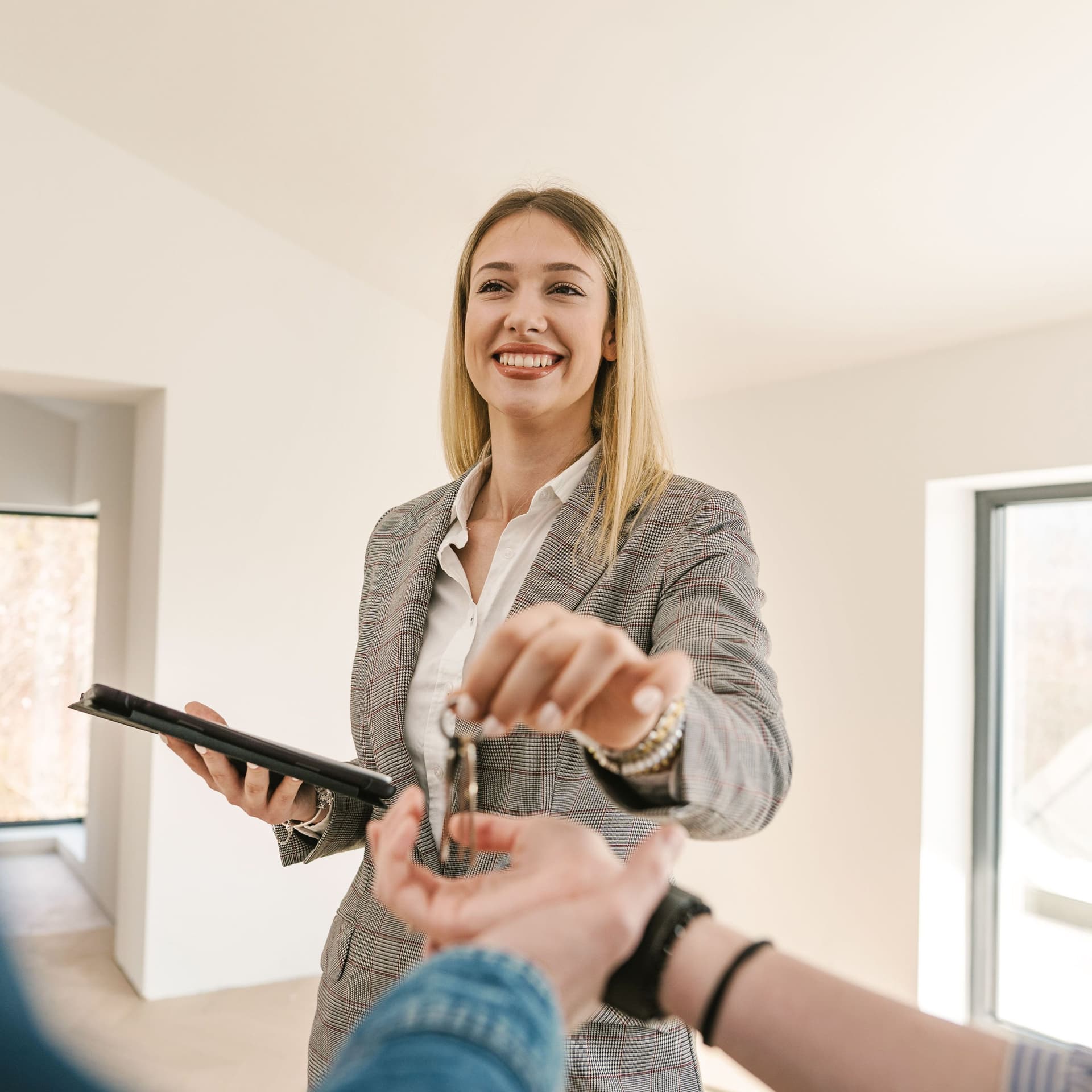 Eine lächelnde Immobilienmaklerin während der Schlüsselübergabe. Im Vordergrund sind zwei Hände zu sehen.