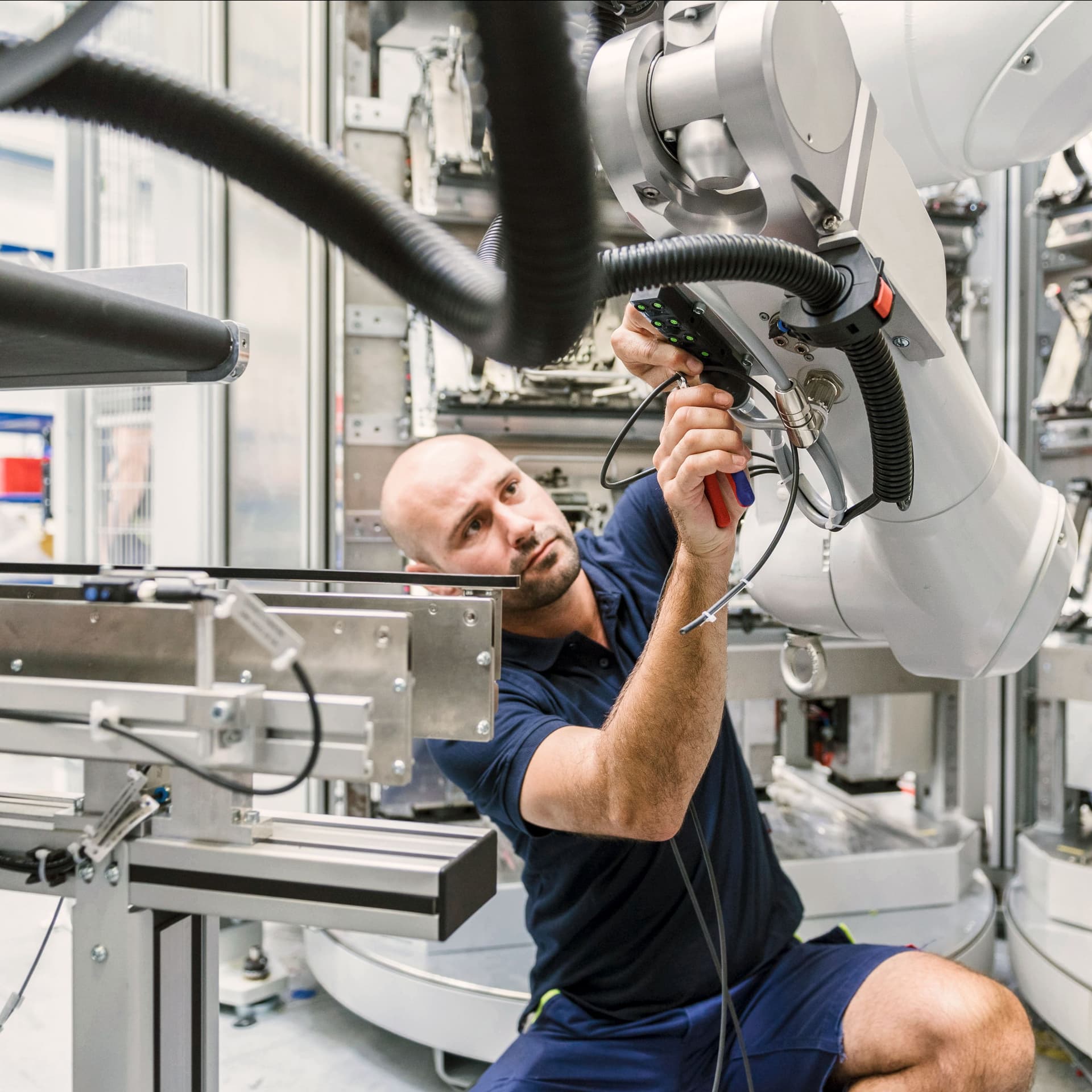 Mann kniet vor Roborterarm in einem modernen und technischen Umfeld und prüft diesen.