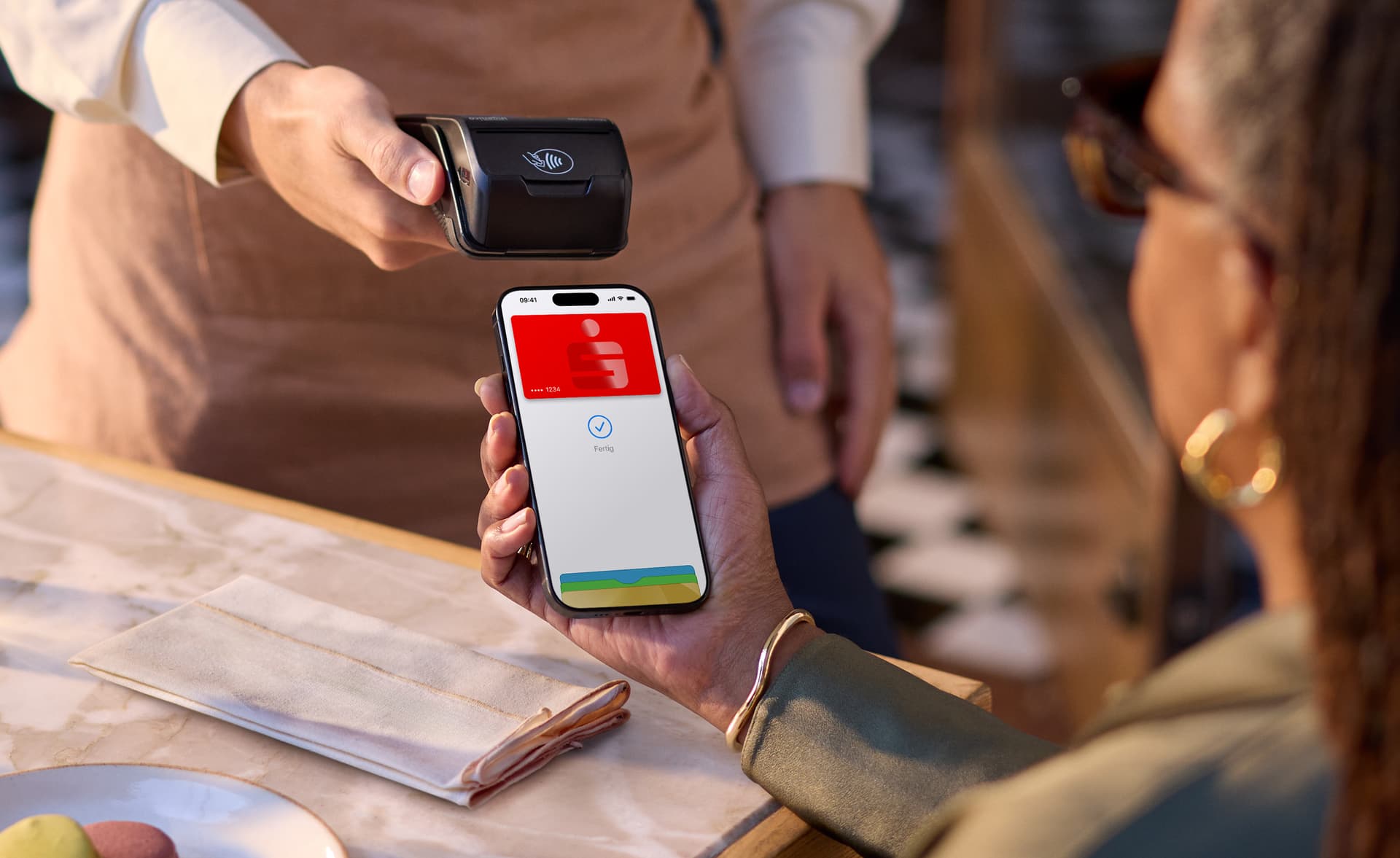 Eine Person zahlt kontaktlos mit einem Smartphone, das eine Sparkassen-Karte anzeigt, an einem Bezahlterminal.