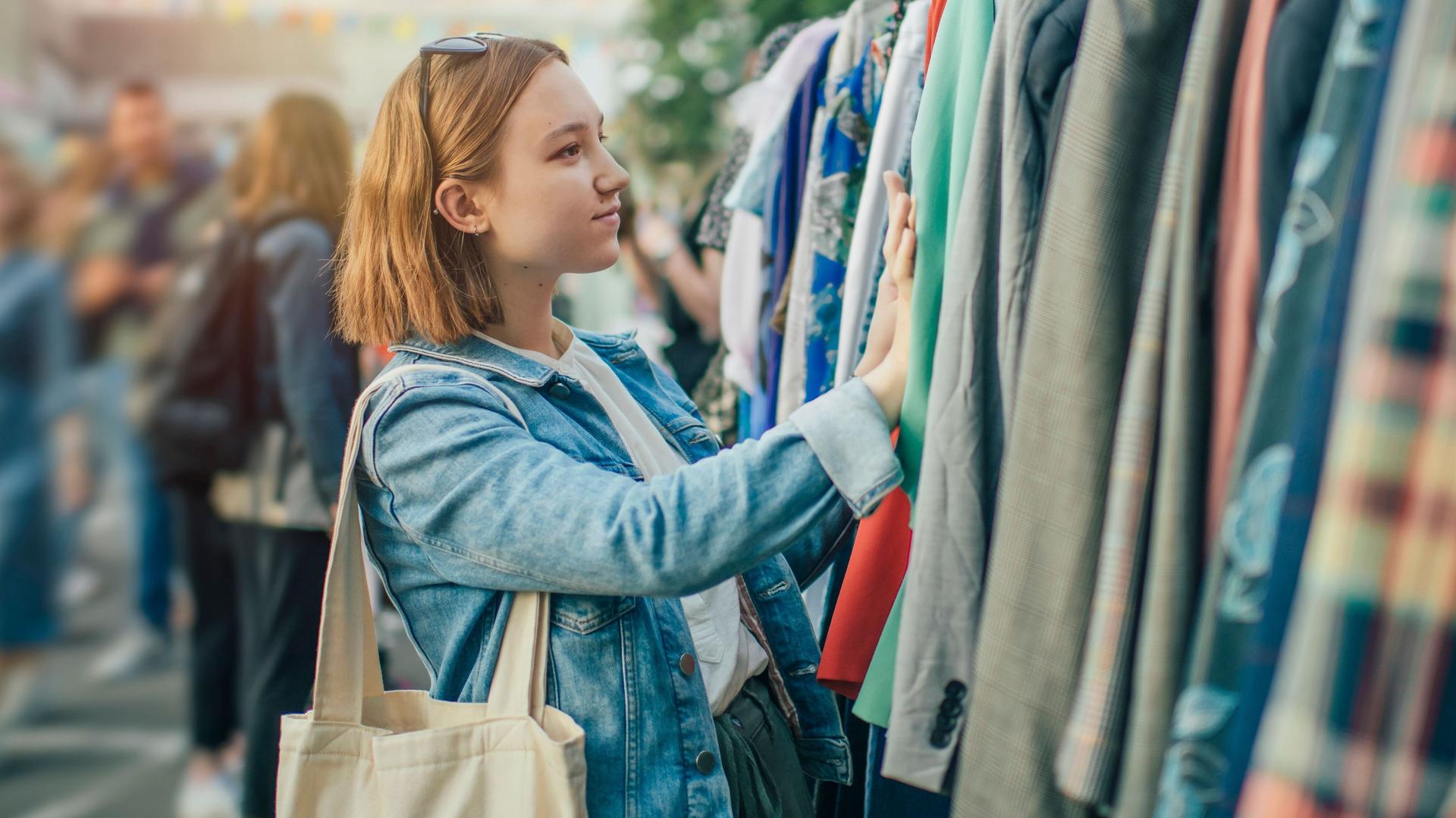 Junge Frau schaut auf einem Flohmarkt nach Jacken auf einem Garderobenständer