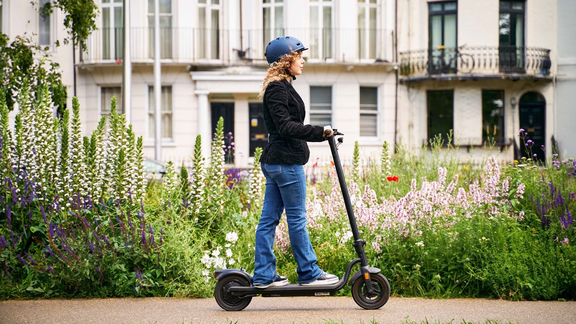 Eine junge Frau fährt mit einem E-Roller durch ein Wohnviertel in einer Großstadt