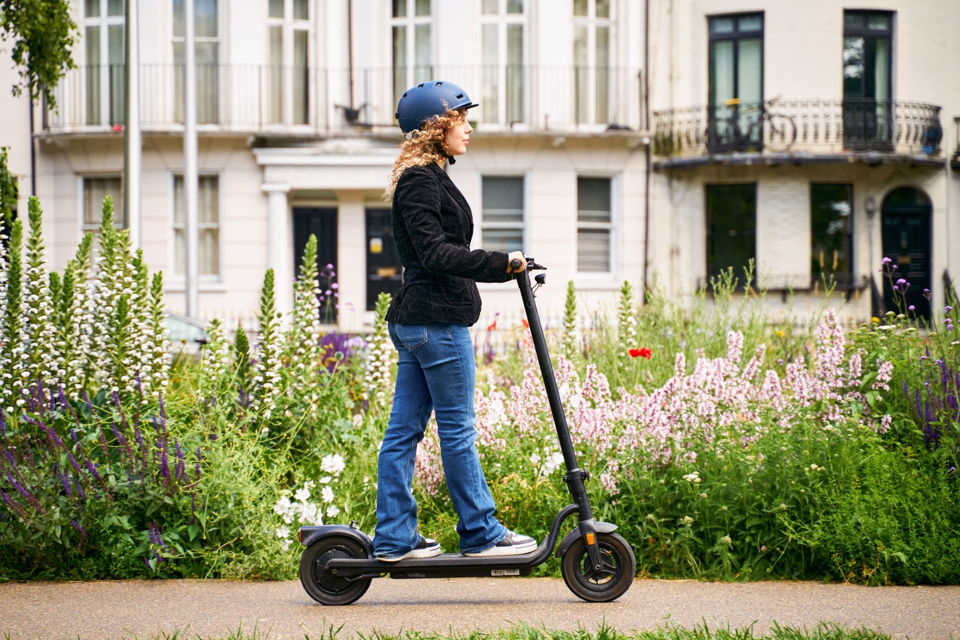Eine junge Frau fährt mit einem E-Roller durch ein Wohnviertel in einer Großstadt