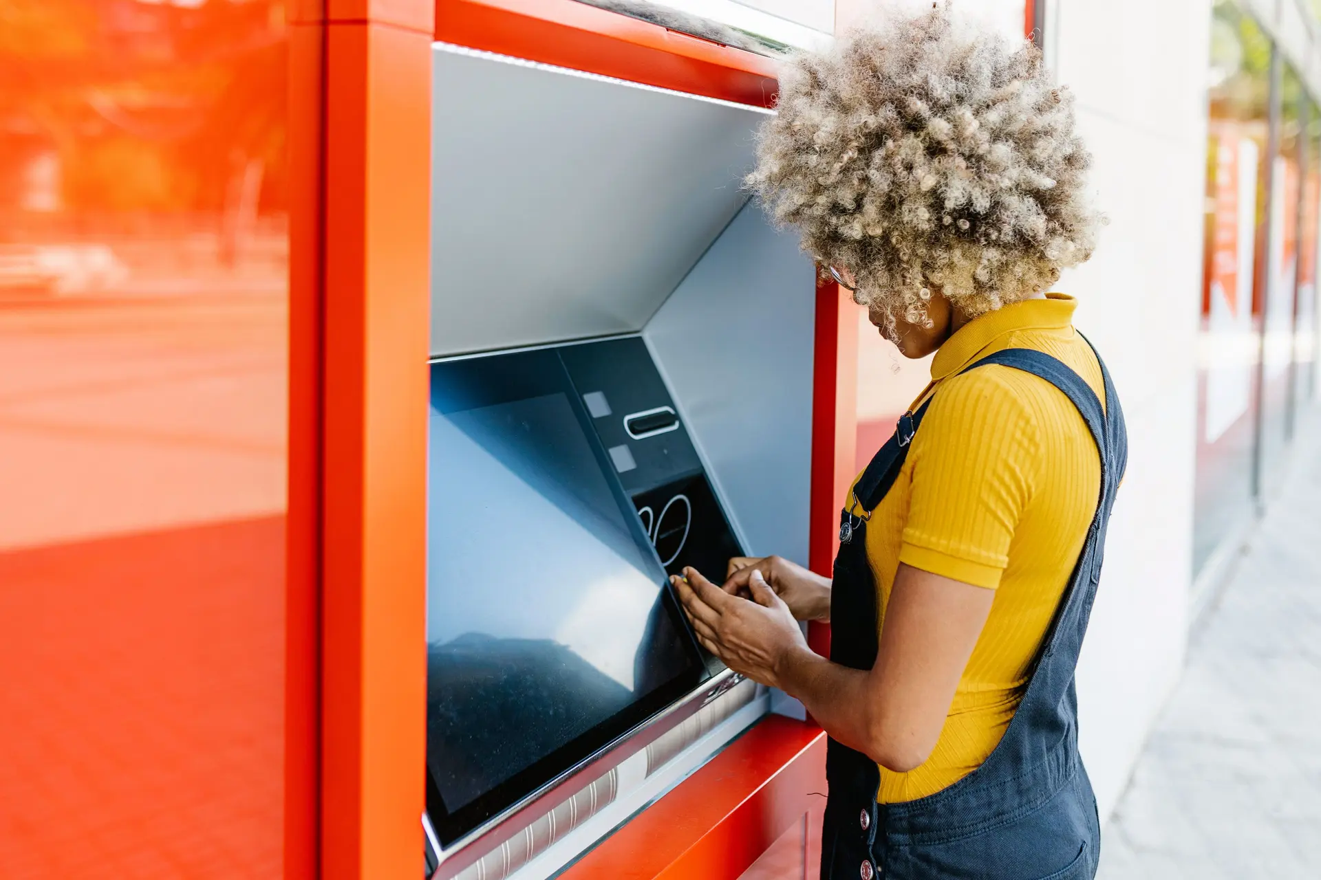 Junge Frau mit Afro hebt an einem Bankautomat Geld ab