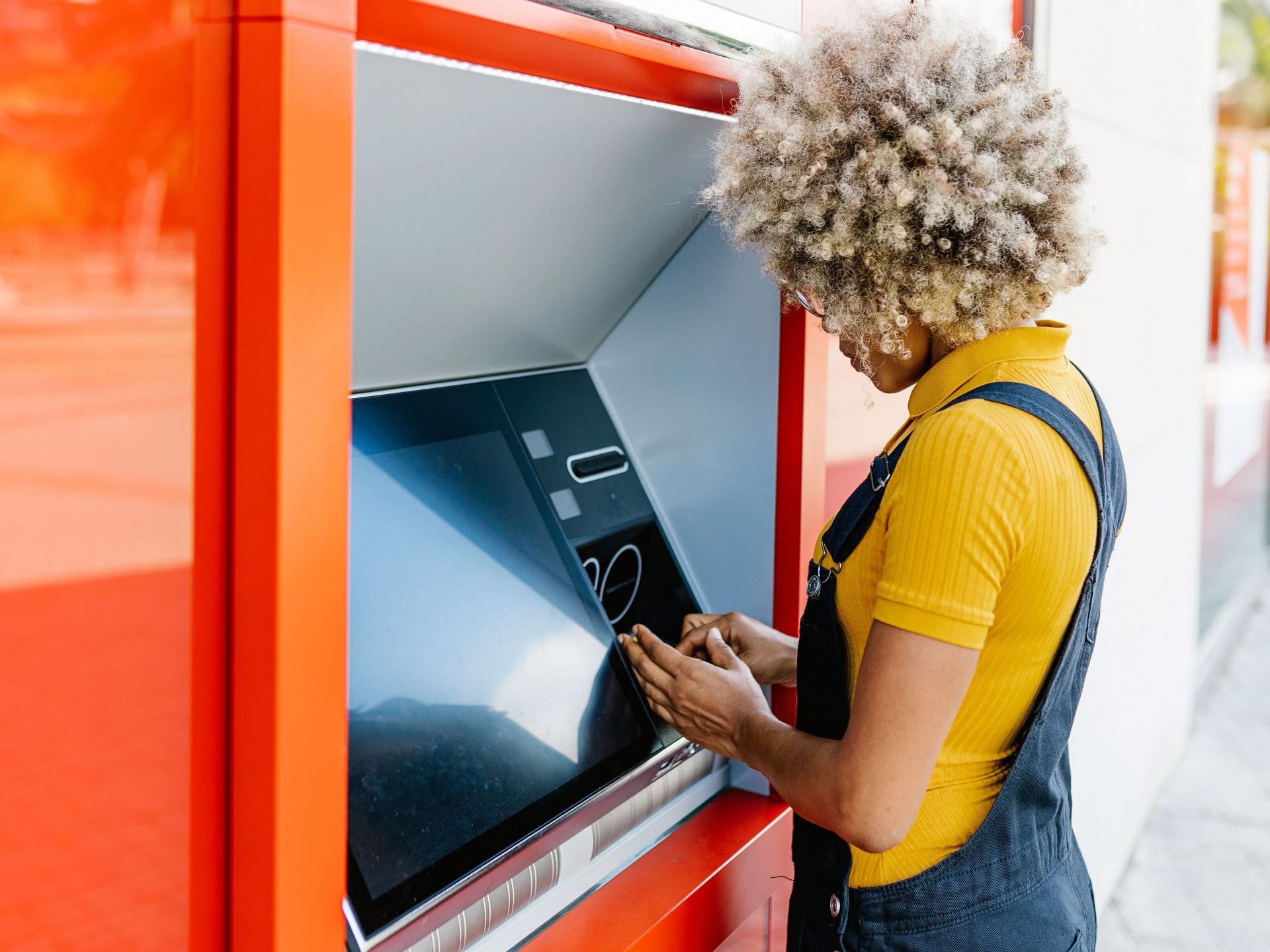 Junge Frau mit Afro hebt an einem Bankautomat Geld ab