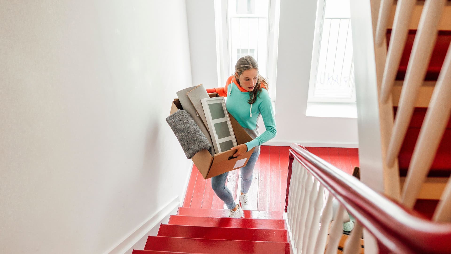 Junge Frau im Treppenhaus trägt Umzugskartons die Treppe hoch