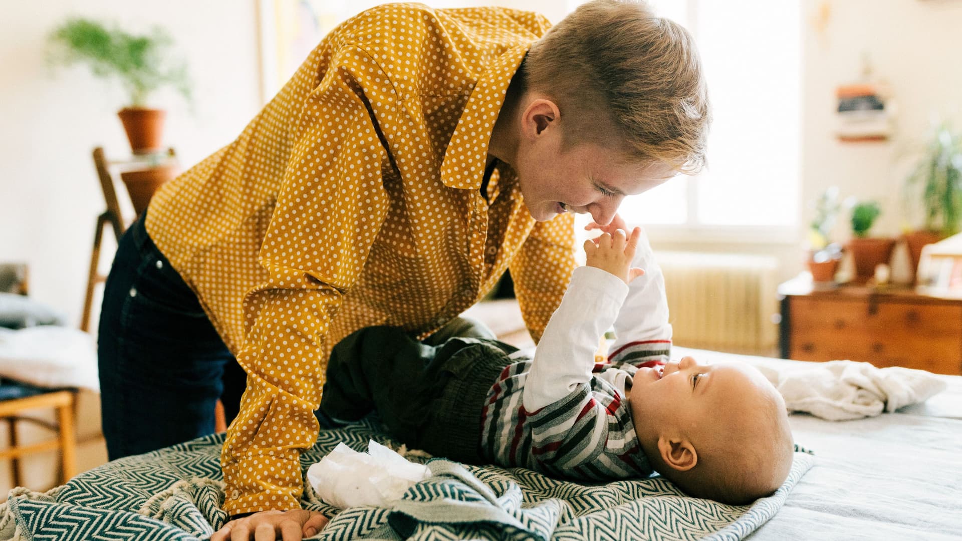 Mutter beugt sich lachend über ihr Baby, das auf dem Bett liegt.