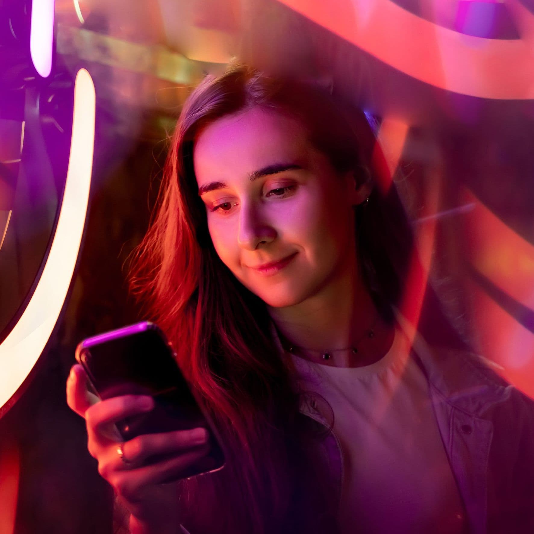 EIne junge Frau schaut auf ein Handy. Um sie herum ist buntes Licht.